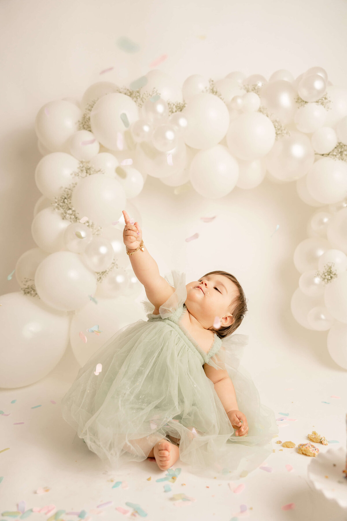 baby girl in green dress pointing at confetti falling in studio mileston picture