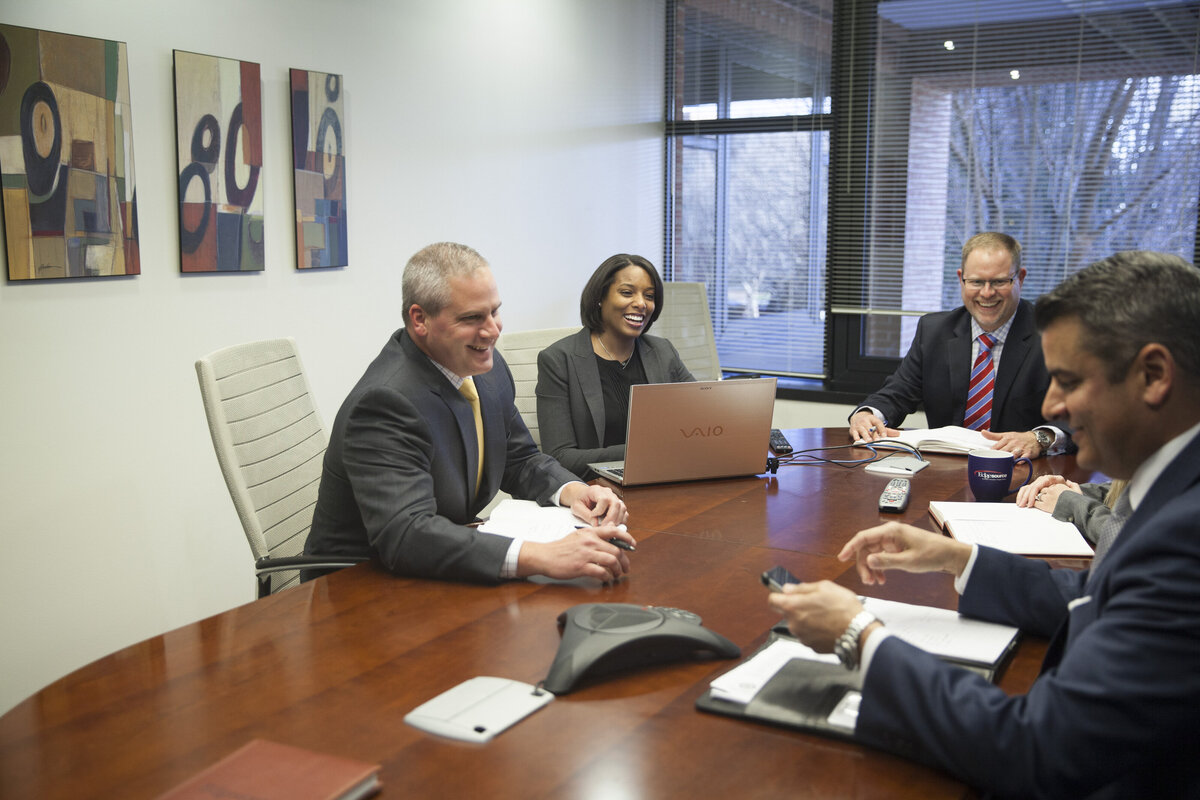 A group of people sit at a wooden table, talking with one another.