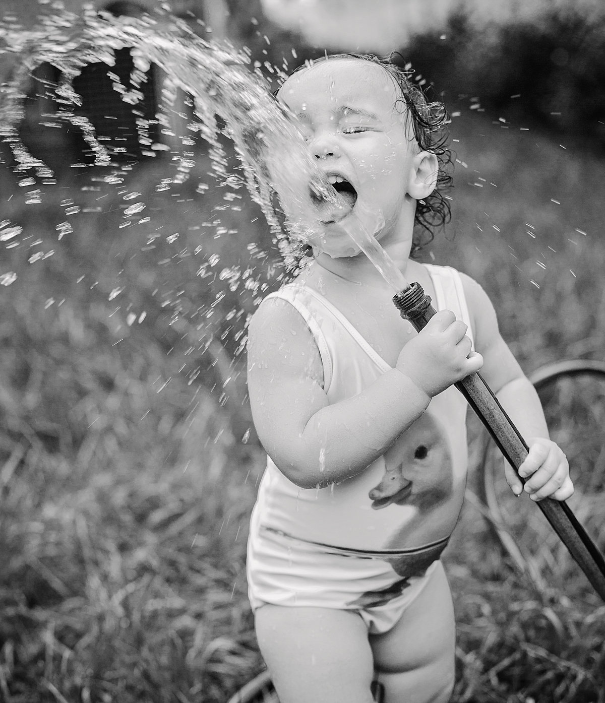 charlotte documentary photographer jamie lucido creates a beautiful and playful image of a small child drinking out of a backyard hose