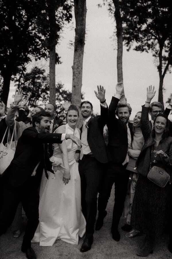 Explosion de rires et d'émotions parmi les invités, les bras levés pour célébrer les mariés qu'ils entourent. Par Kamescop, photographe mariage vintage.