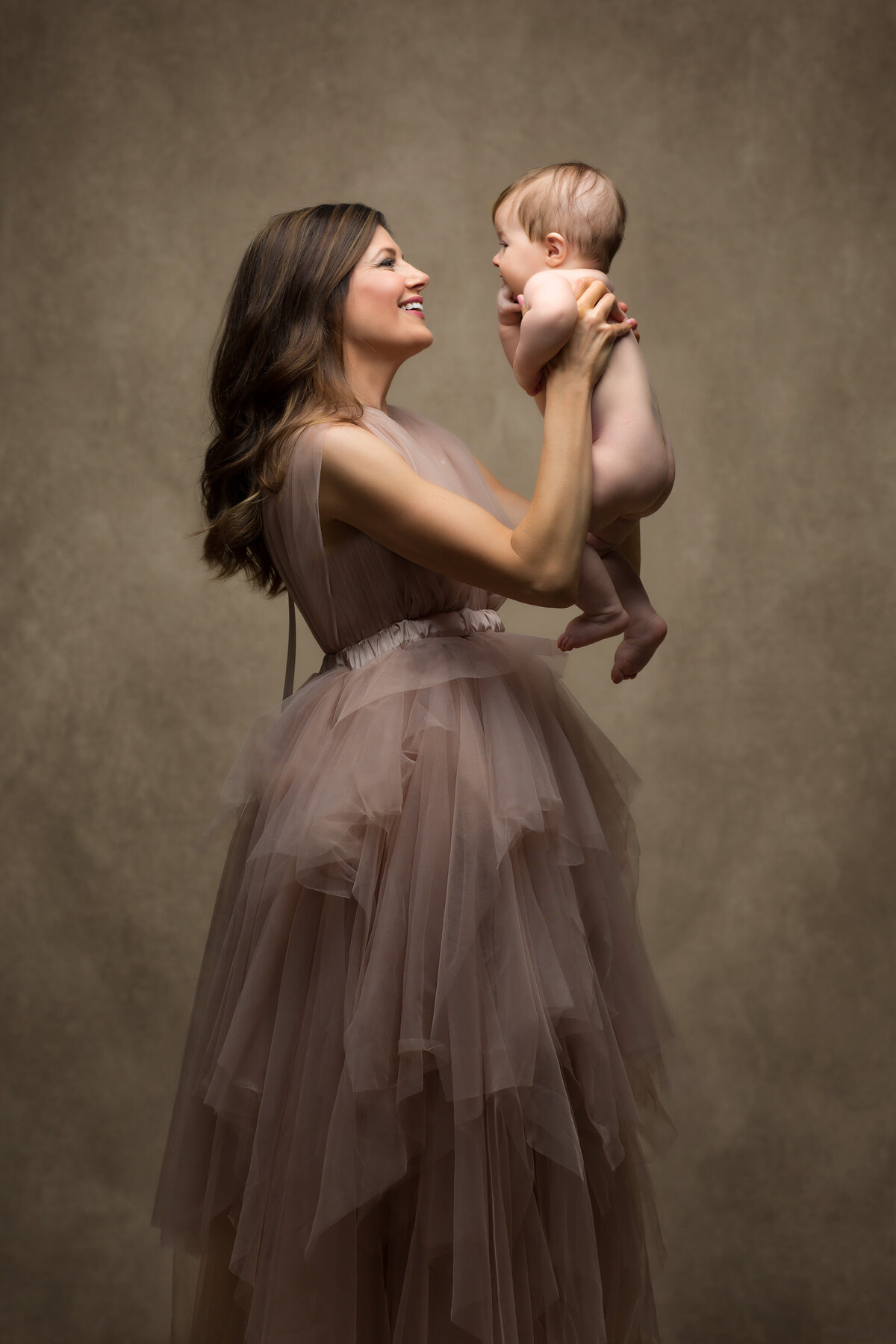 A joyful mother lifts her baby in a loving embrace, captured by a Dallas family photographer.
