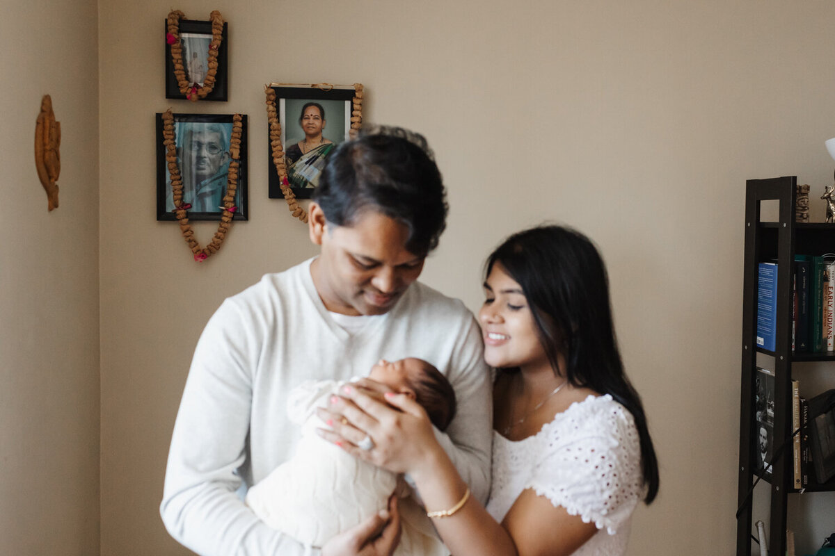 Indian parents standing in front of special shrine to family members while holding newborn daughter during Toronto Newborn Photography session