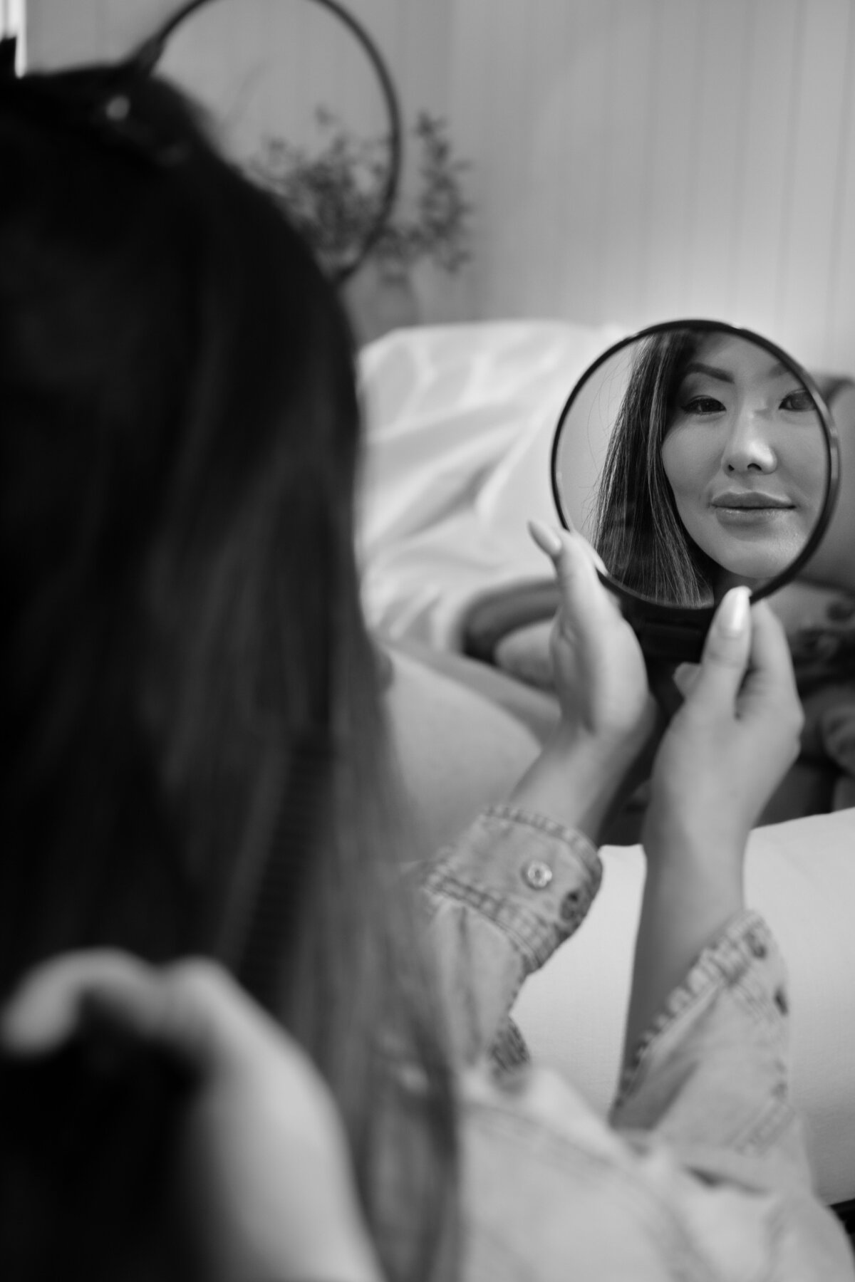 B&W Asian Lady looking at her reflection in hand mirror.