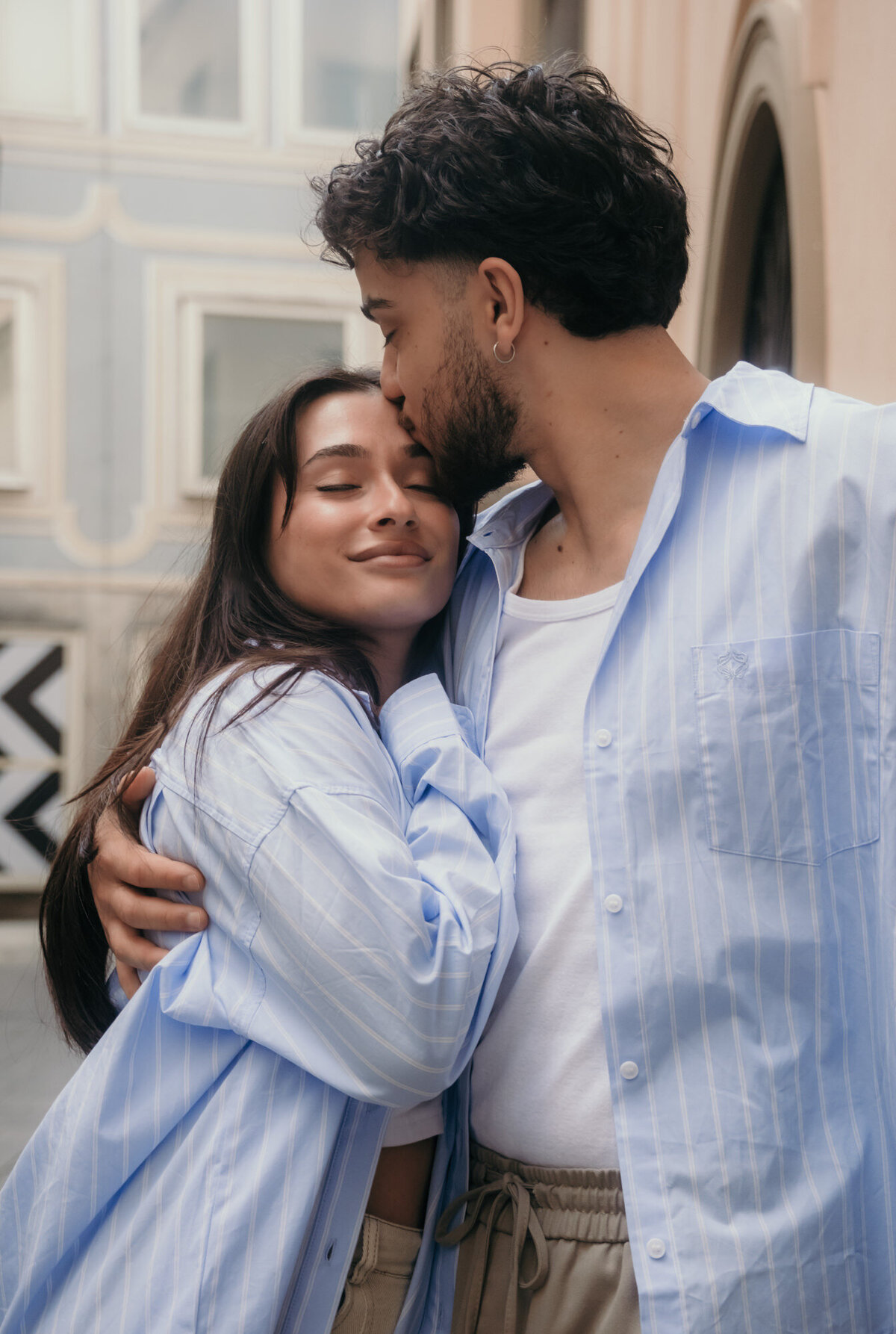 Couple in matching colors hugs while he kisses her on the forehad.