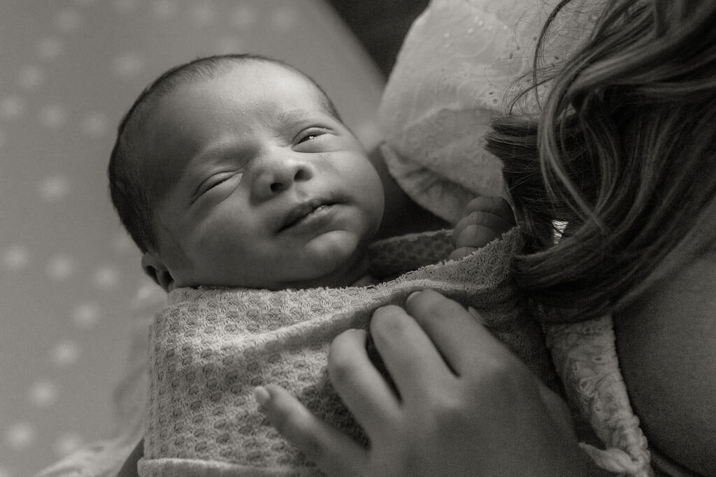 Newborn baby swaddled and resting on mother’s chest during a natural light lifestyle session in Miami, Florida.