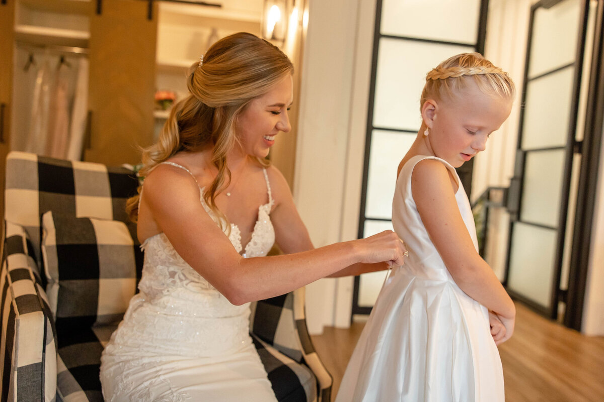 bride helps tie bow of flower girl's dress at Milestone Georgetown wedding in Texas