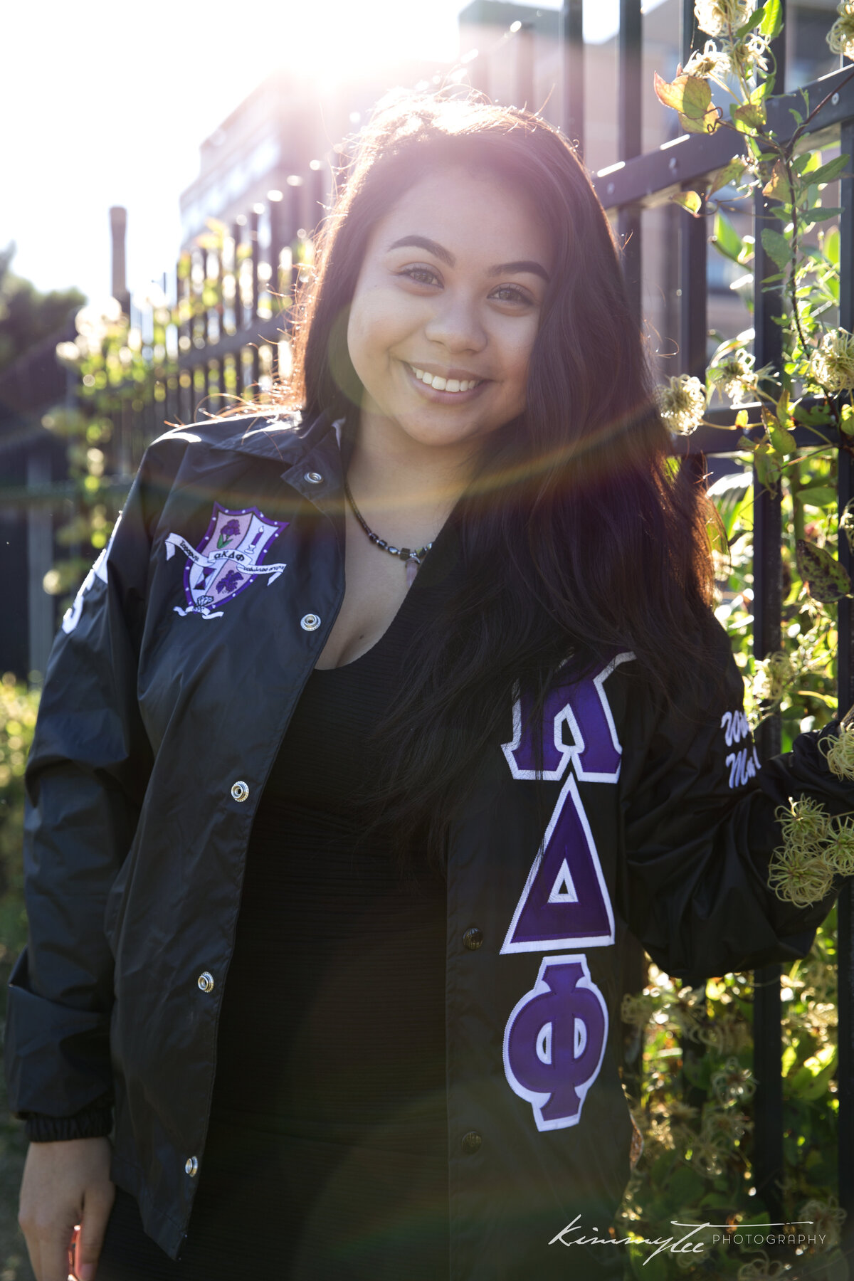 Smiling sorority girl holding onto fence wearing line jacket