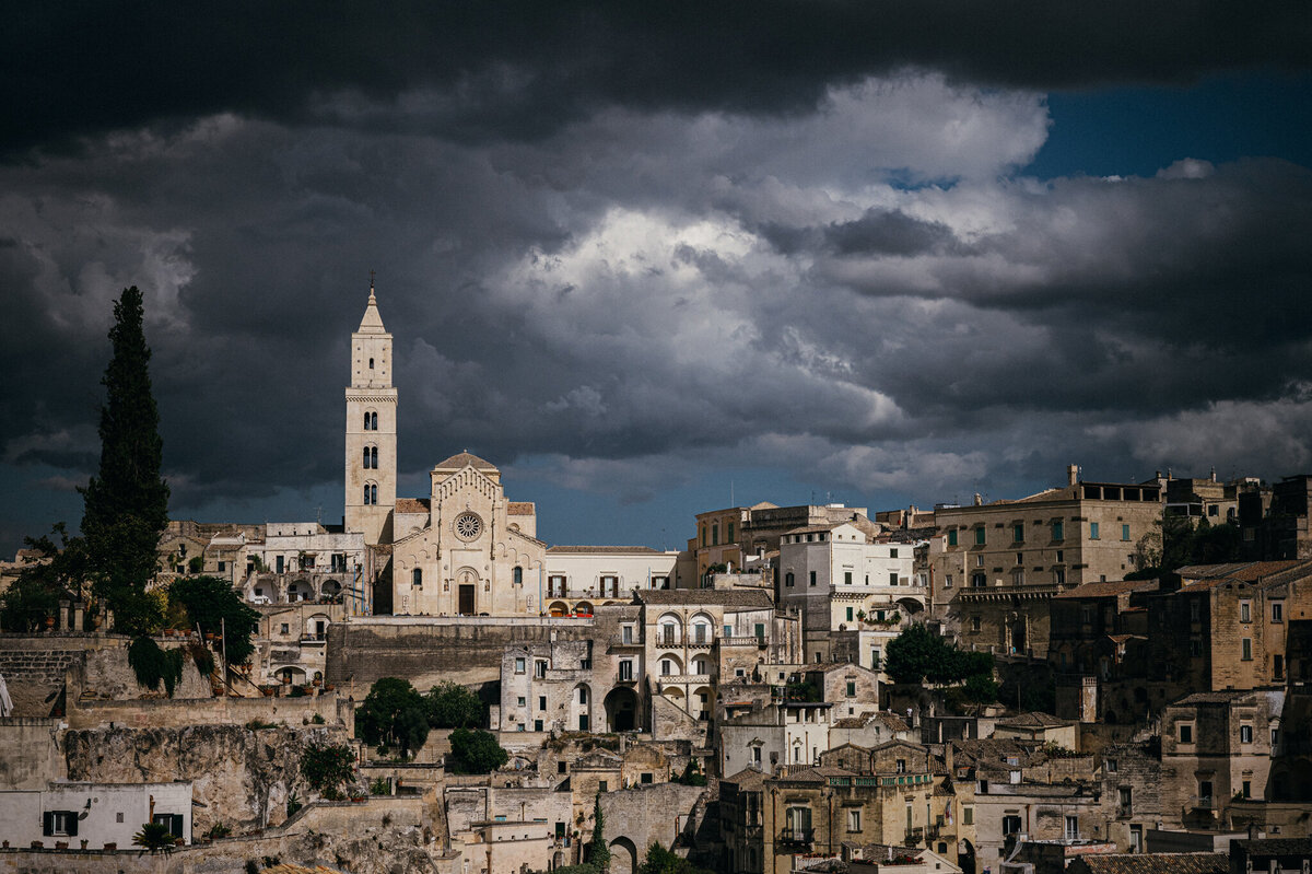 Looking into the Sassi of Matera, the houses, buildings and churches are all carved out of the calcarenite rock of the region. Storm clouds are overhead but the sun shines on the city