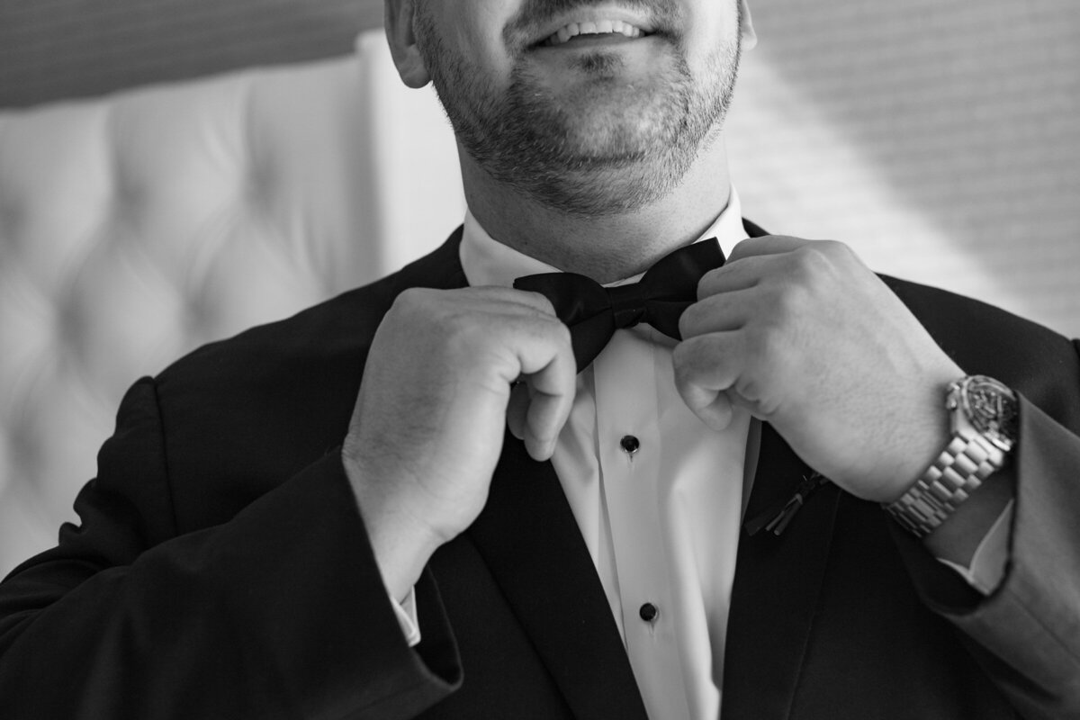 black and white close up of the groom adjusting his bow tie at The Adolphus in Dallas, highlighting elegant wedding preparation details.