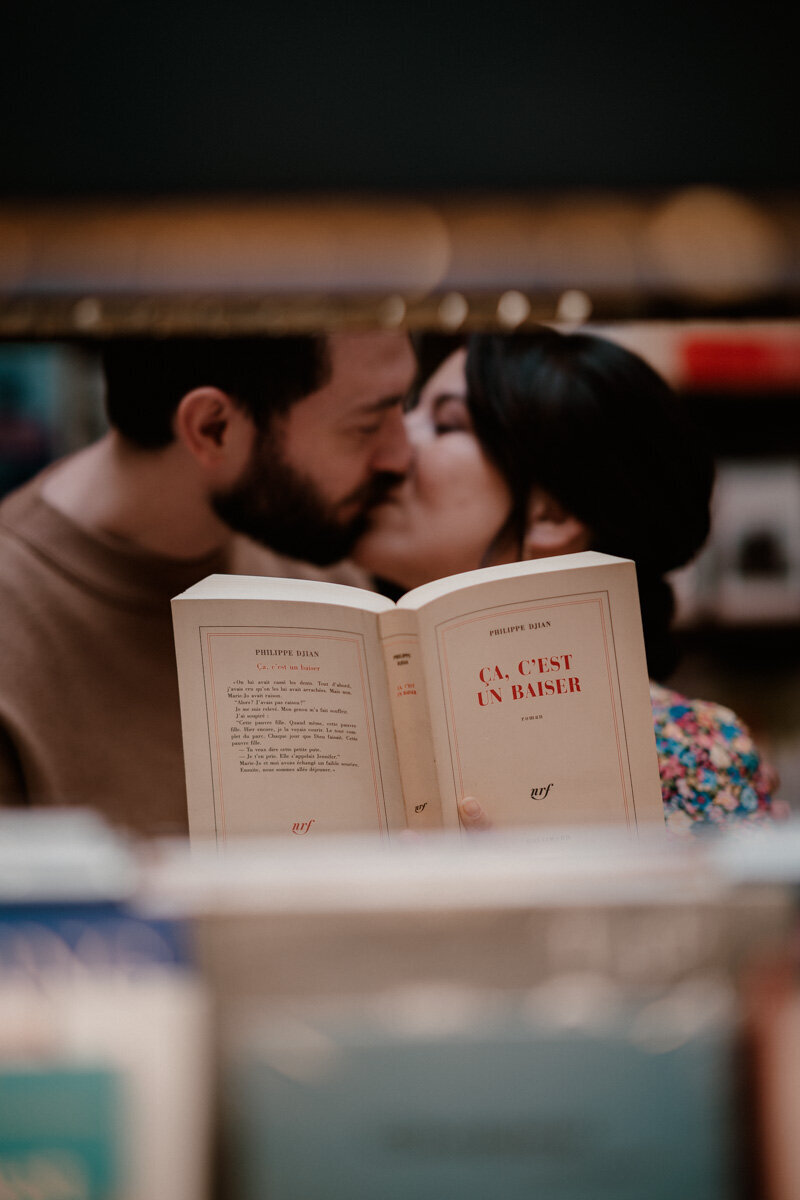 Un couple échange un baiser derrière un livre intitulé “Ça, c’est un baiser” lors d’une séance photo à la Librairie Galignani à Paris.