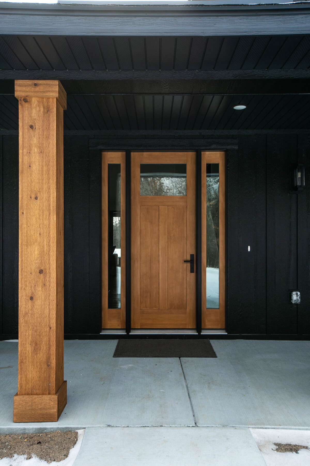 Exterior view of custom home in Elk River, Minnesota with black siding, wood details and front porch built by Cornerstone Custom Builds