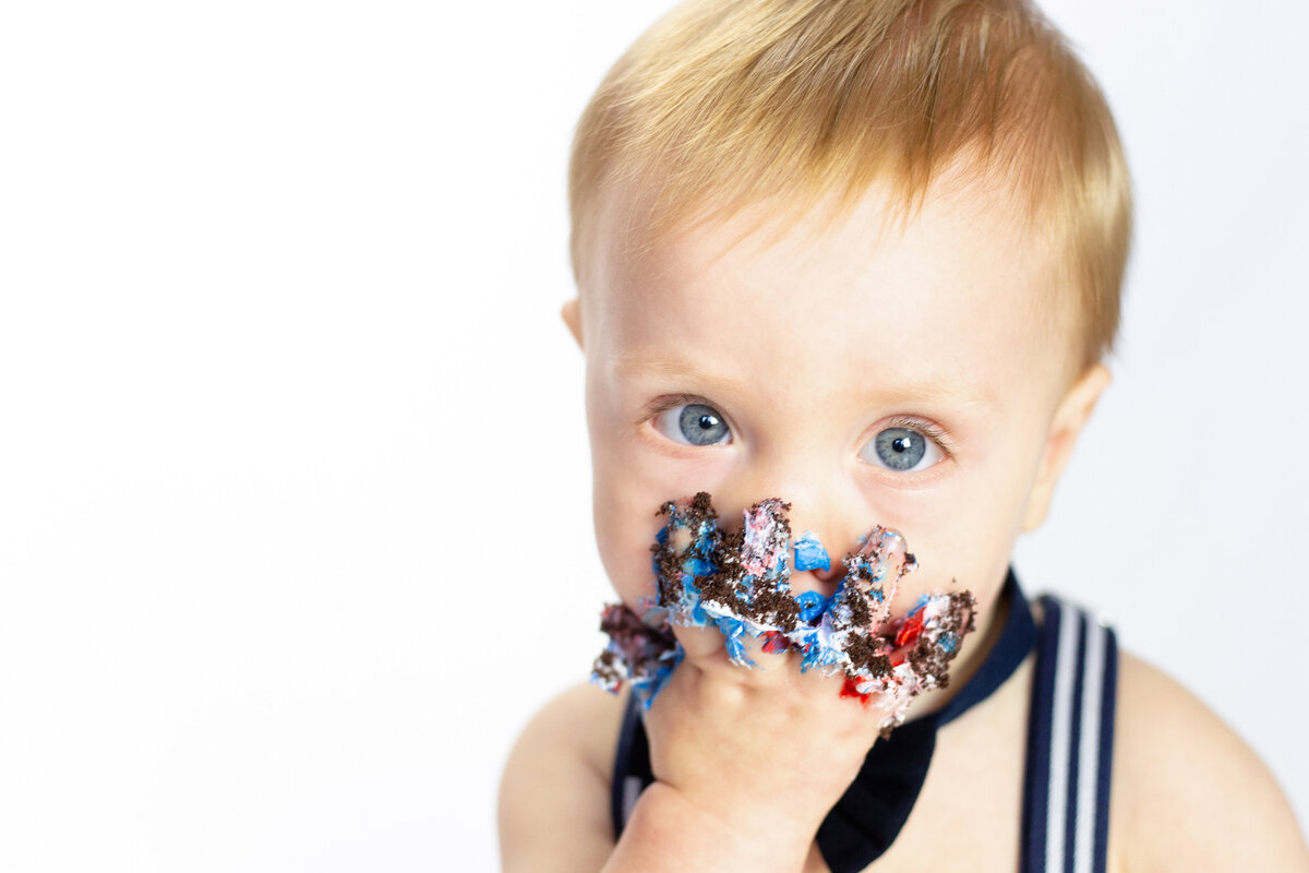 blue eyed baby shoves frosting covered hand in mouth