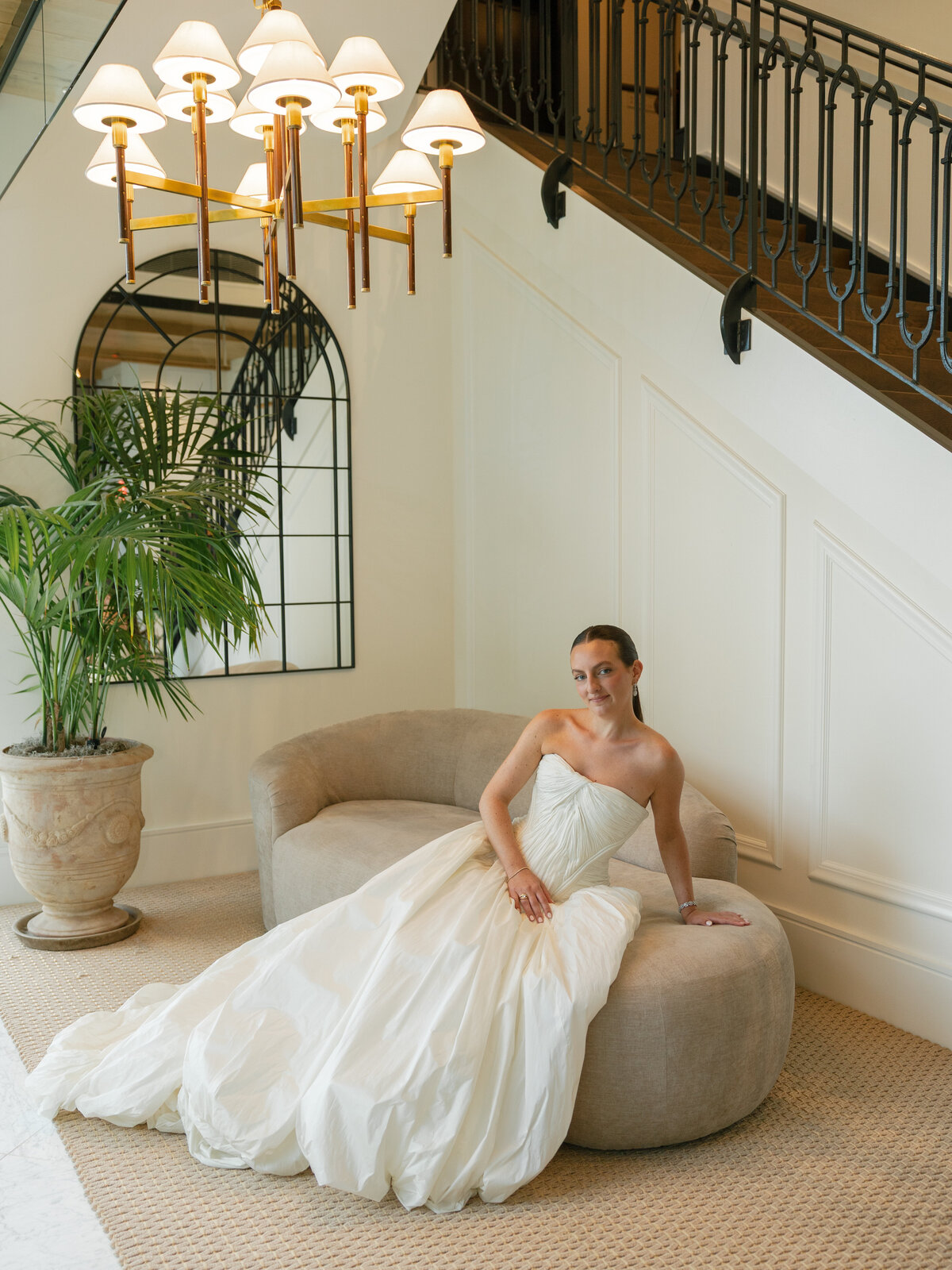 Kara in her gown resting on a curved sofa beneath the chandelier at Pendry Natirar