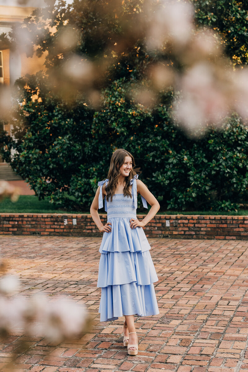 Girl in blue dress standing with her hands on her hips gazing into the distance