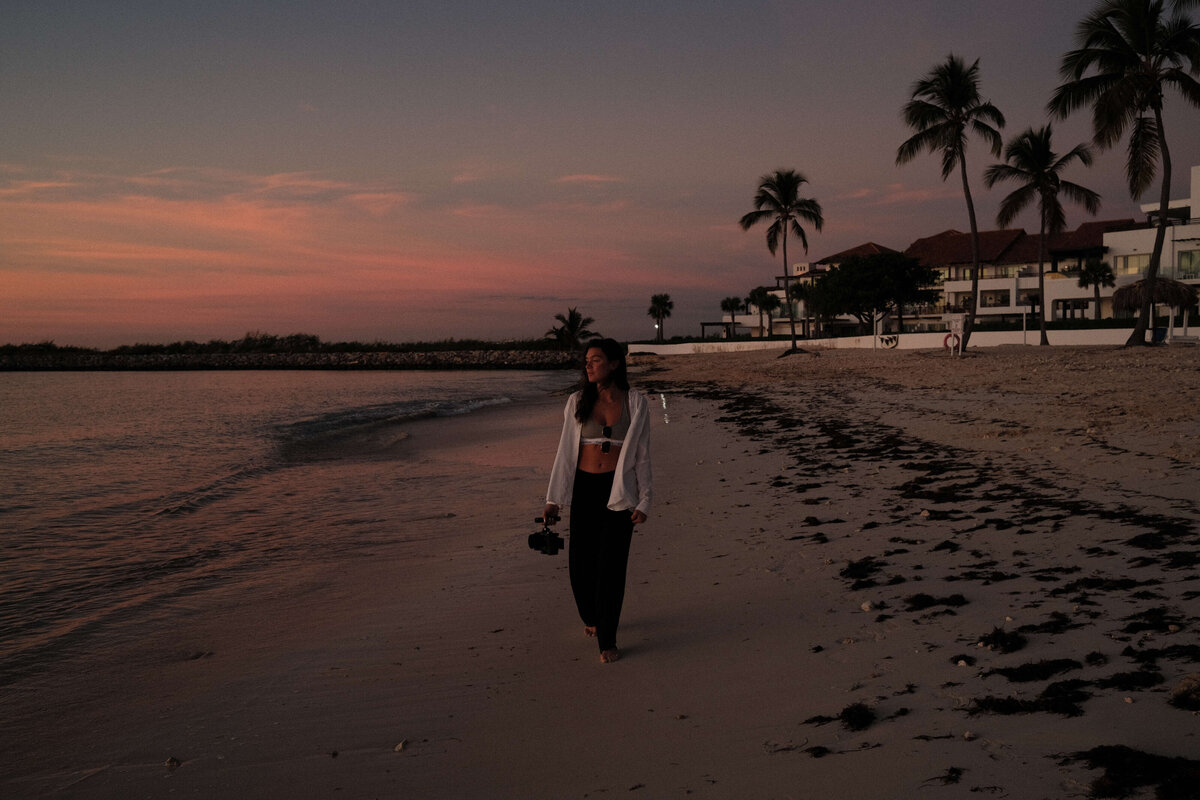 Girl walking down beach with camera in hand