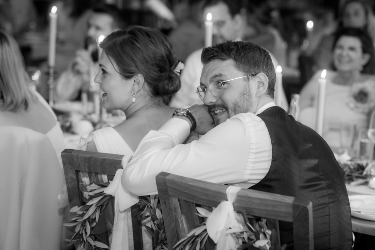 Das Hochzeitspaar lauscht einer Rede. Der Bräutigam blickt über die Schulter in die Kamera.