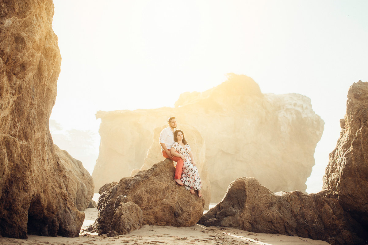Engagement Photograph Of  Man And Woman Looking Up While Seated On a Rock Formation Los Angeles