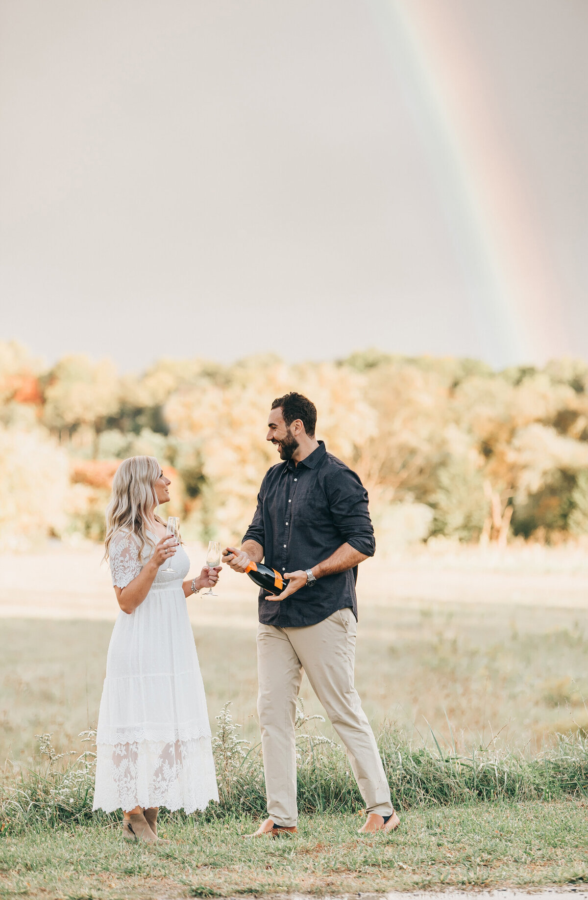 Couple popping champaign under a rainbow at their summer engagement session in London Ontario
