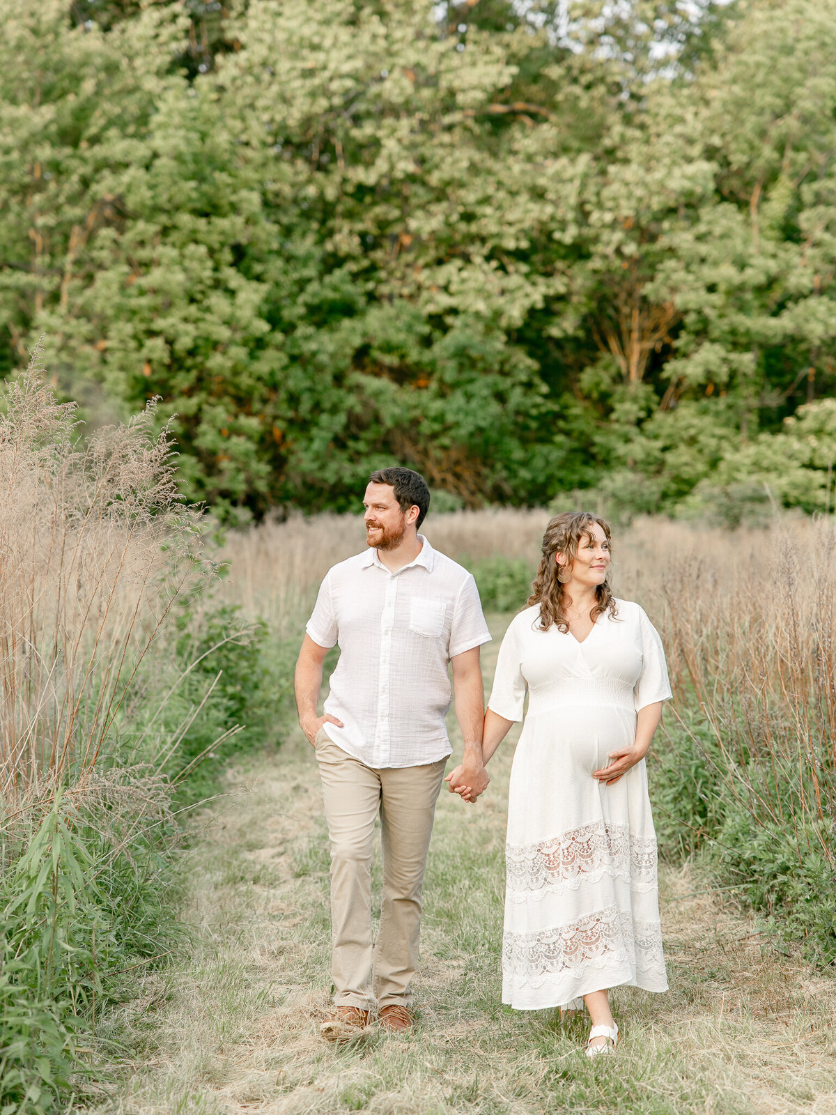 a couple walking holding hands while woman cradles her pregnant belly