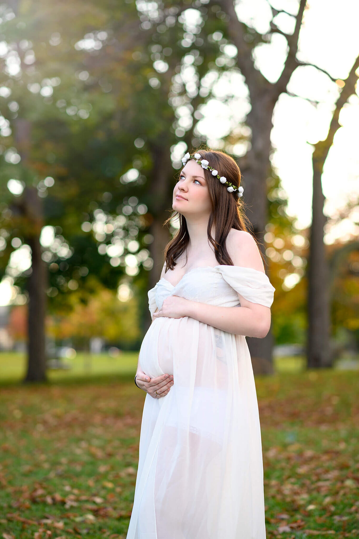 Outdoor maternity portrait of beautiful mom in white gown and crown holding her belly.