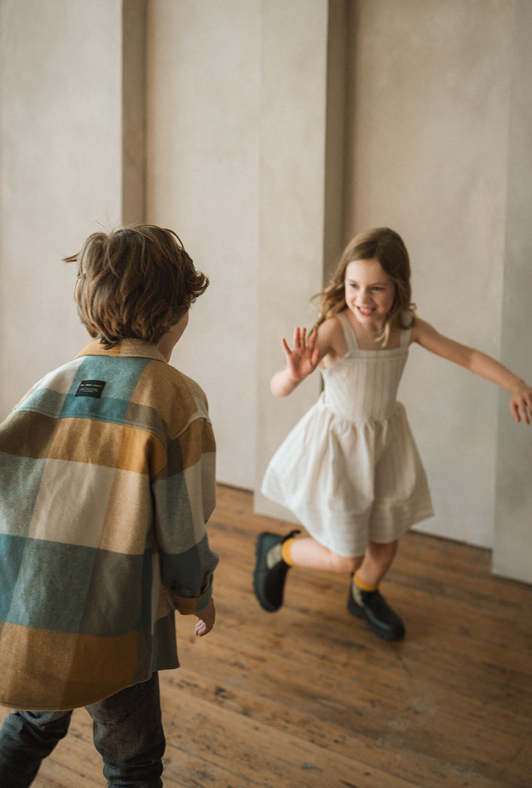 Children running toward each other in a neutral-toned studio, playful movement and soft natural light.