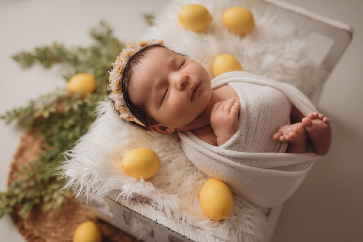 Newborn photo shoot at Marietta GA photography studio with newborn girl laying in little bed wrapped in swaddle with lemon decorations around her