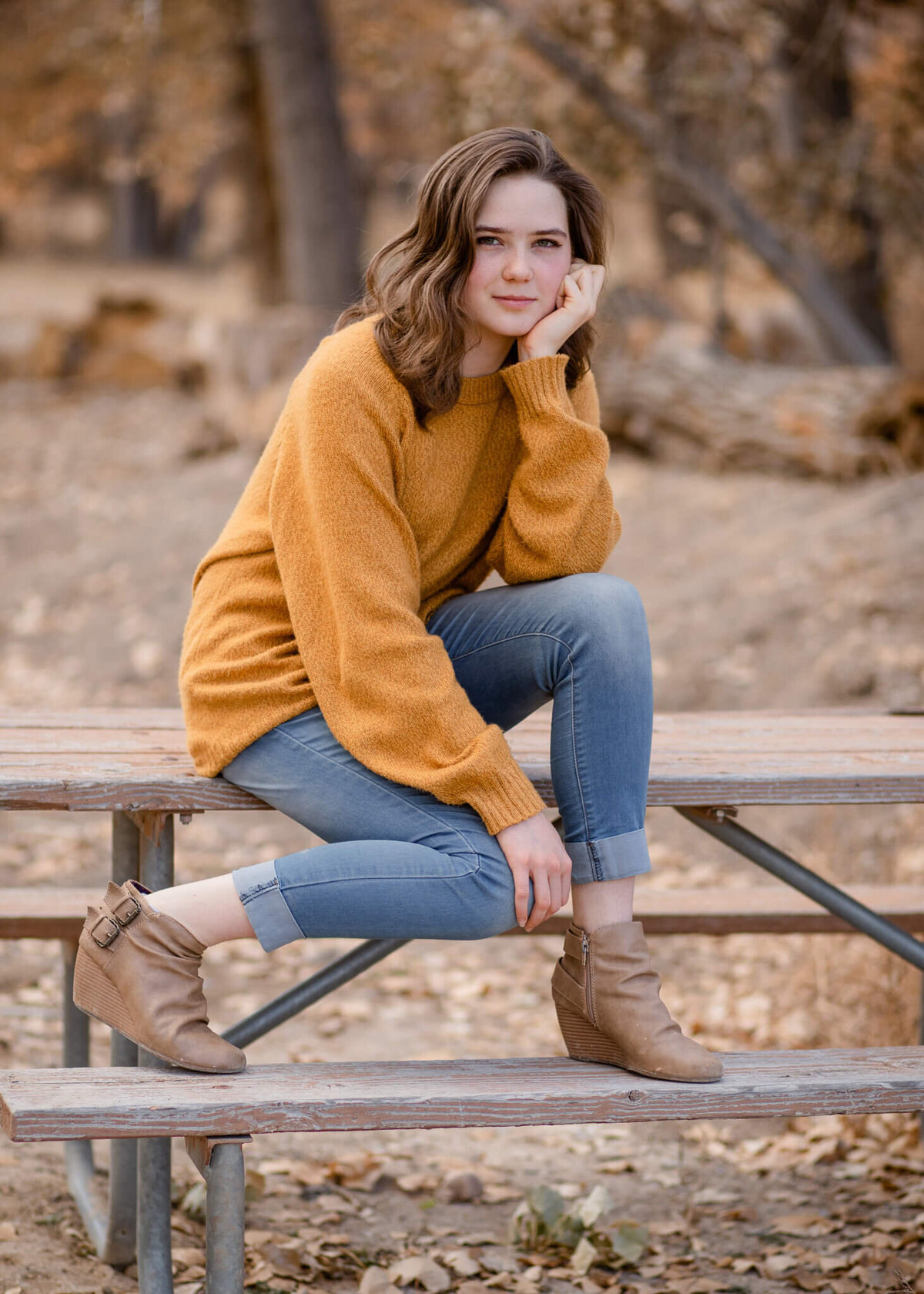 high school senior girl sitting on a picnic table wearing a yellow sweater and jeans