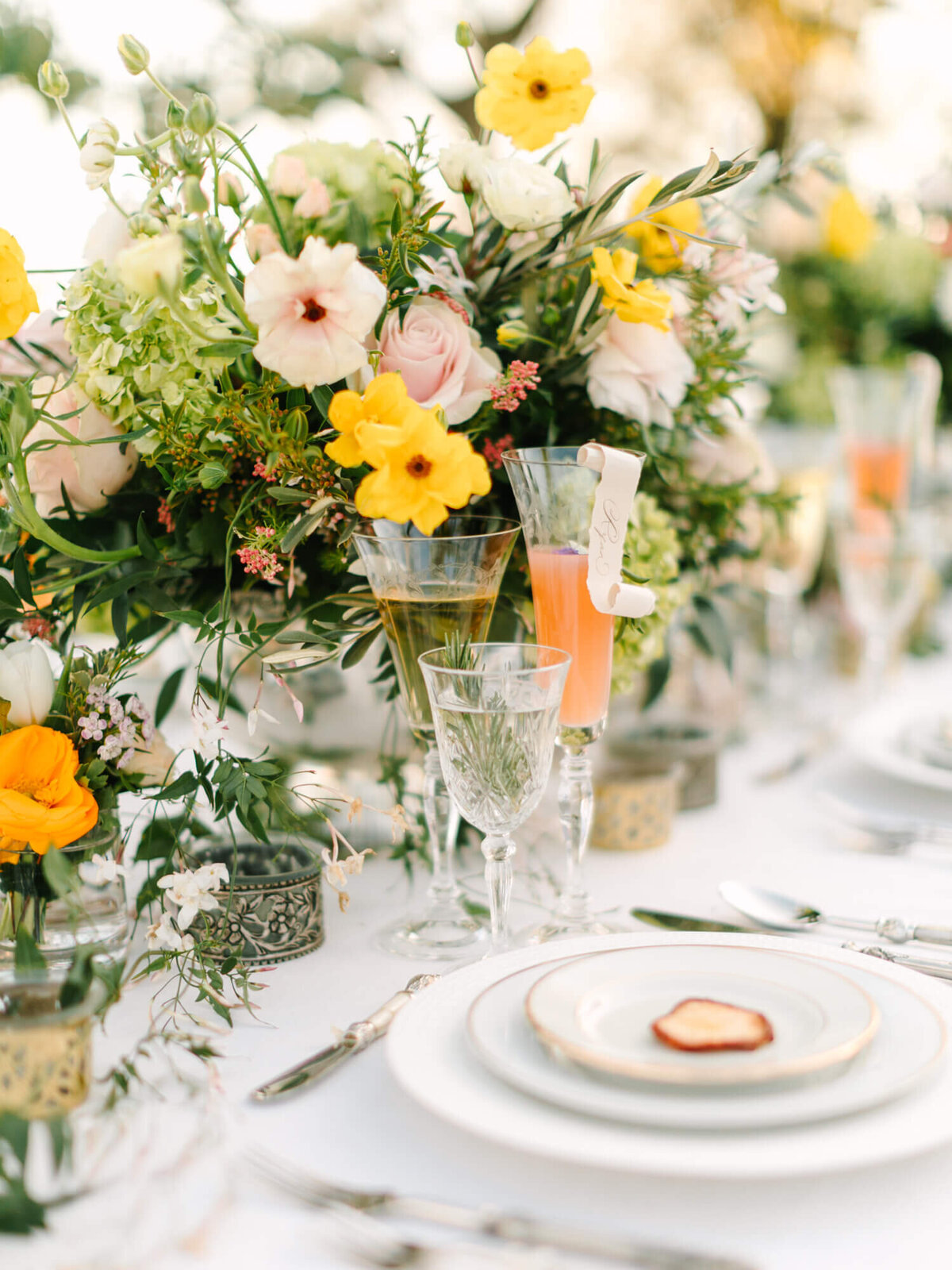 Elegant table setting with a pastel-hued floral centerpiece, and glasses of orange and clear drinks.