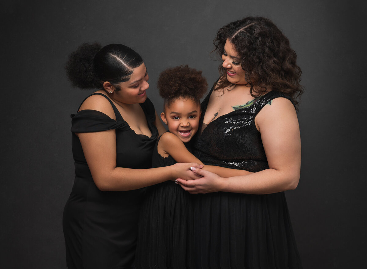 A loving studio portrait of two women and a young girl in black dresses