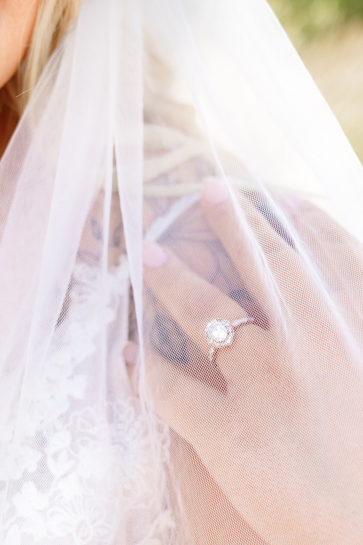 A close-up of the bride’s hand resting against her veil, showcasing her sparkling engagement ring with intricate details.