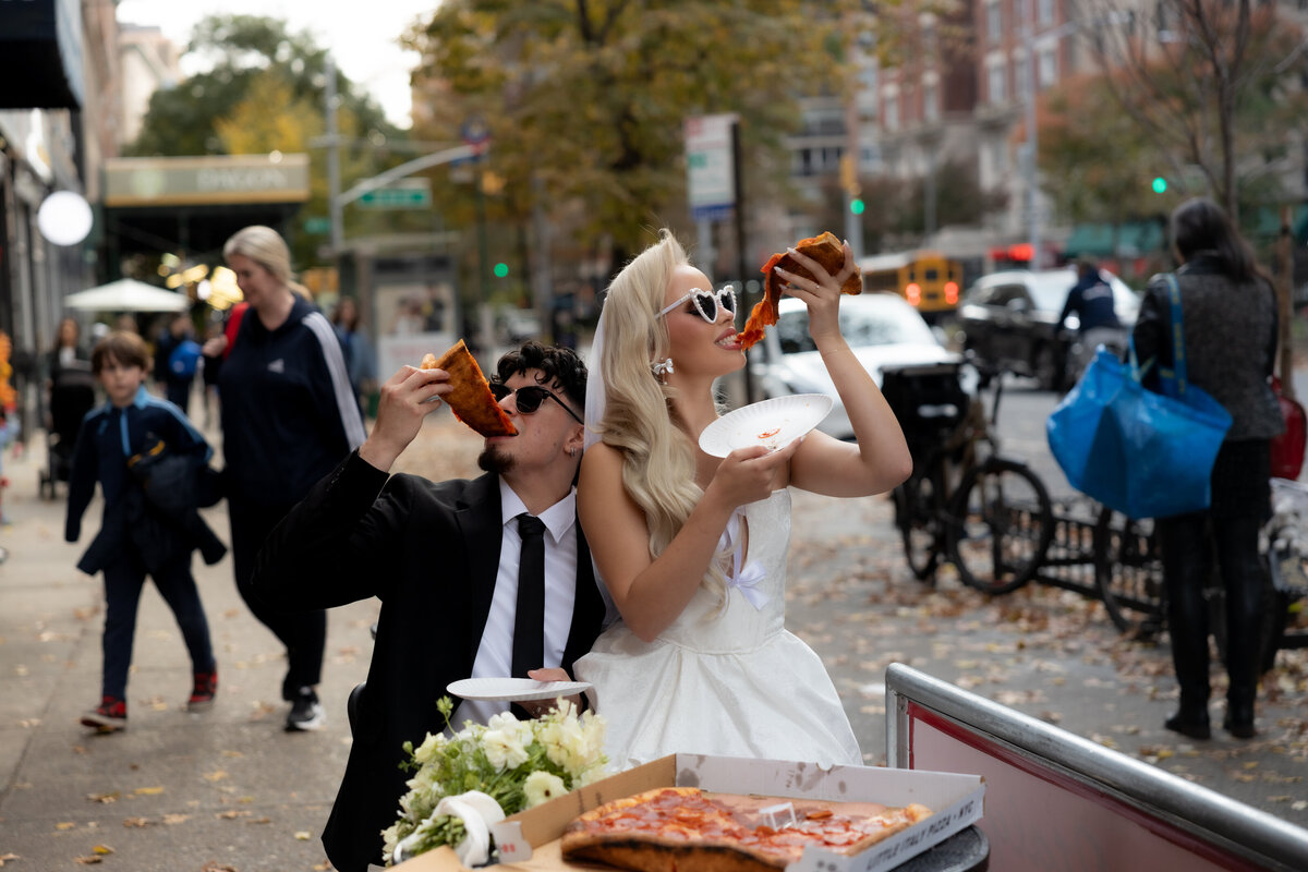 Bride and groom toasting their pizza slices together in celebration of their NYC elopement.
