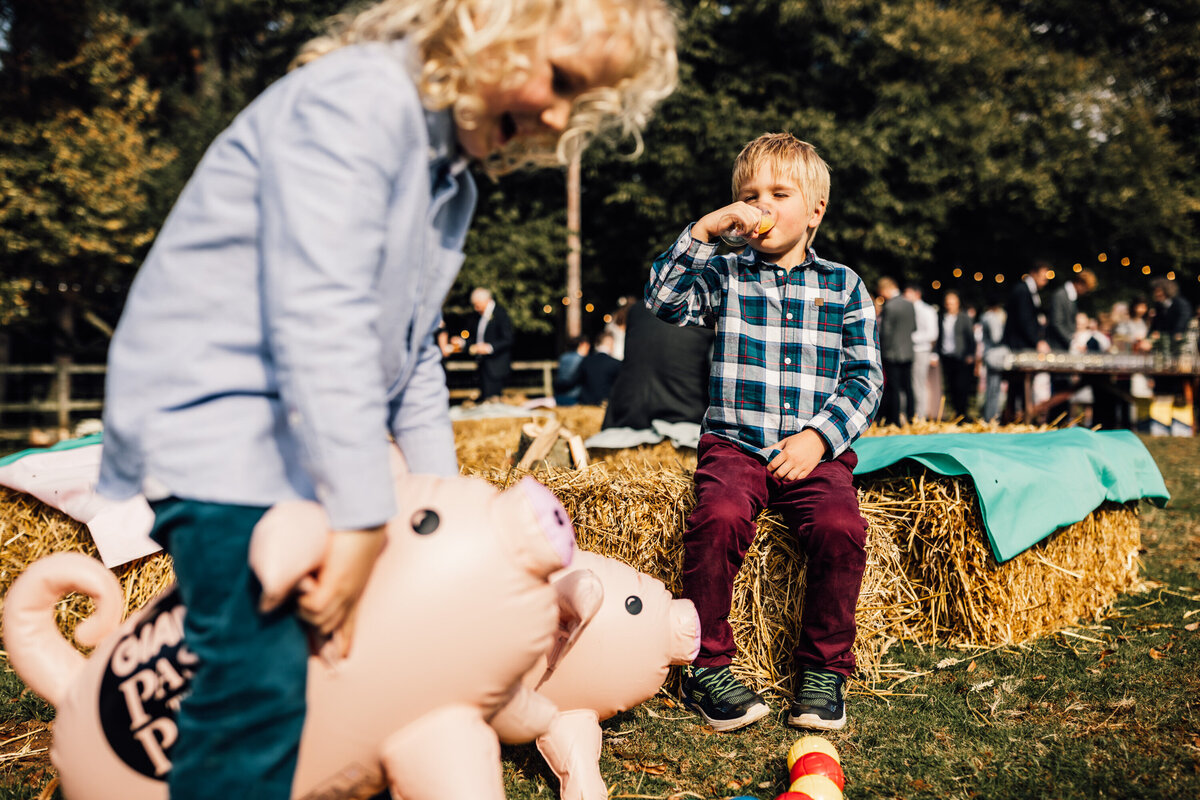 Kids enjoying outdoor wedding with hay bales and pigs