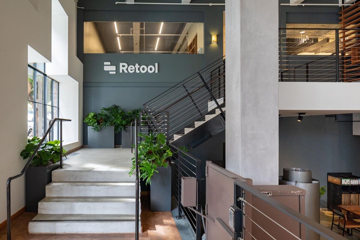 Retool office entrance featuring a concrete staircase, large indoor plants, steel railings, and the Retool logo displayed on a dark gray wall.