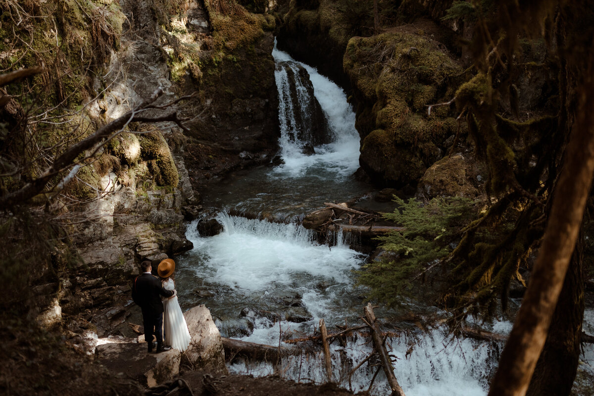 bride and groom posing by waterfall