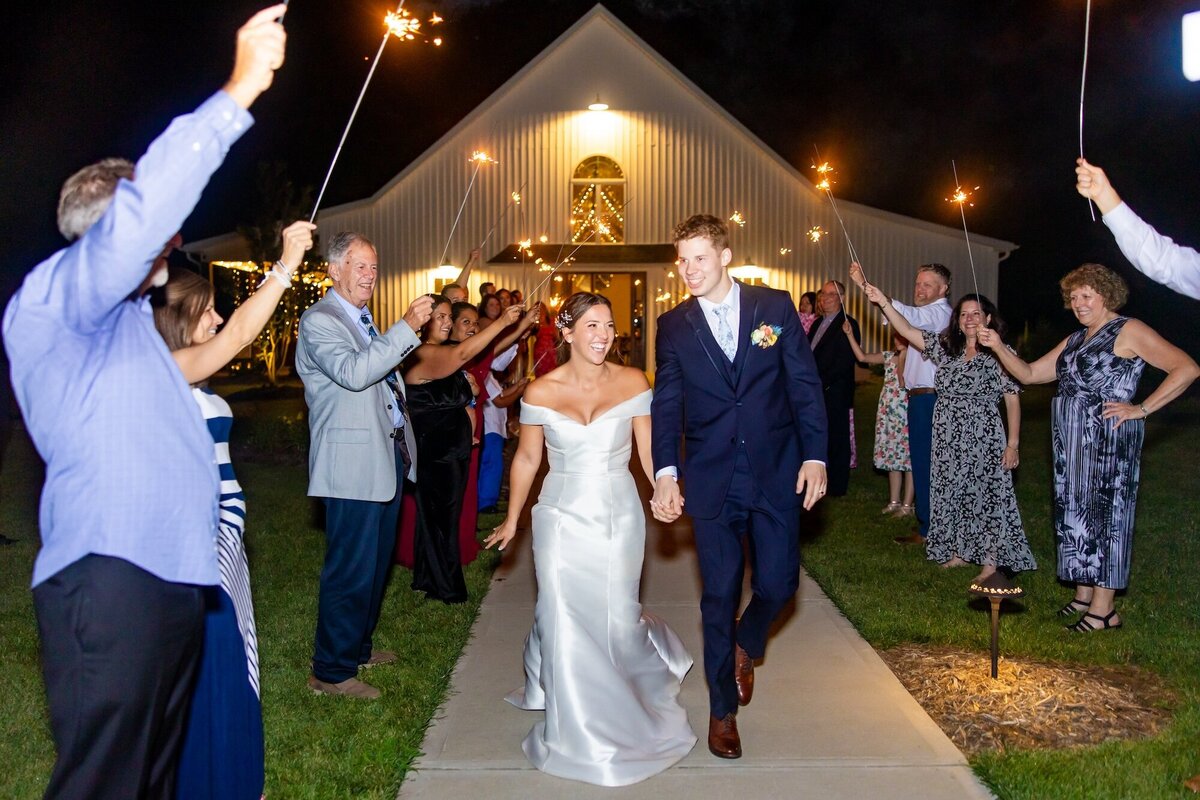 Bride and groom walking as guests twirl sparklers during sendoff