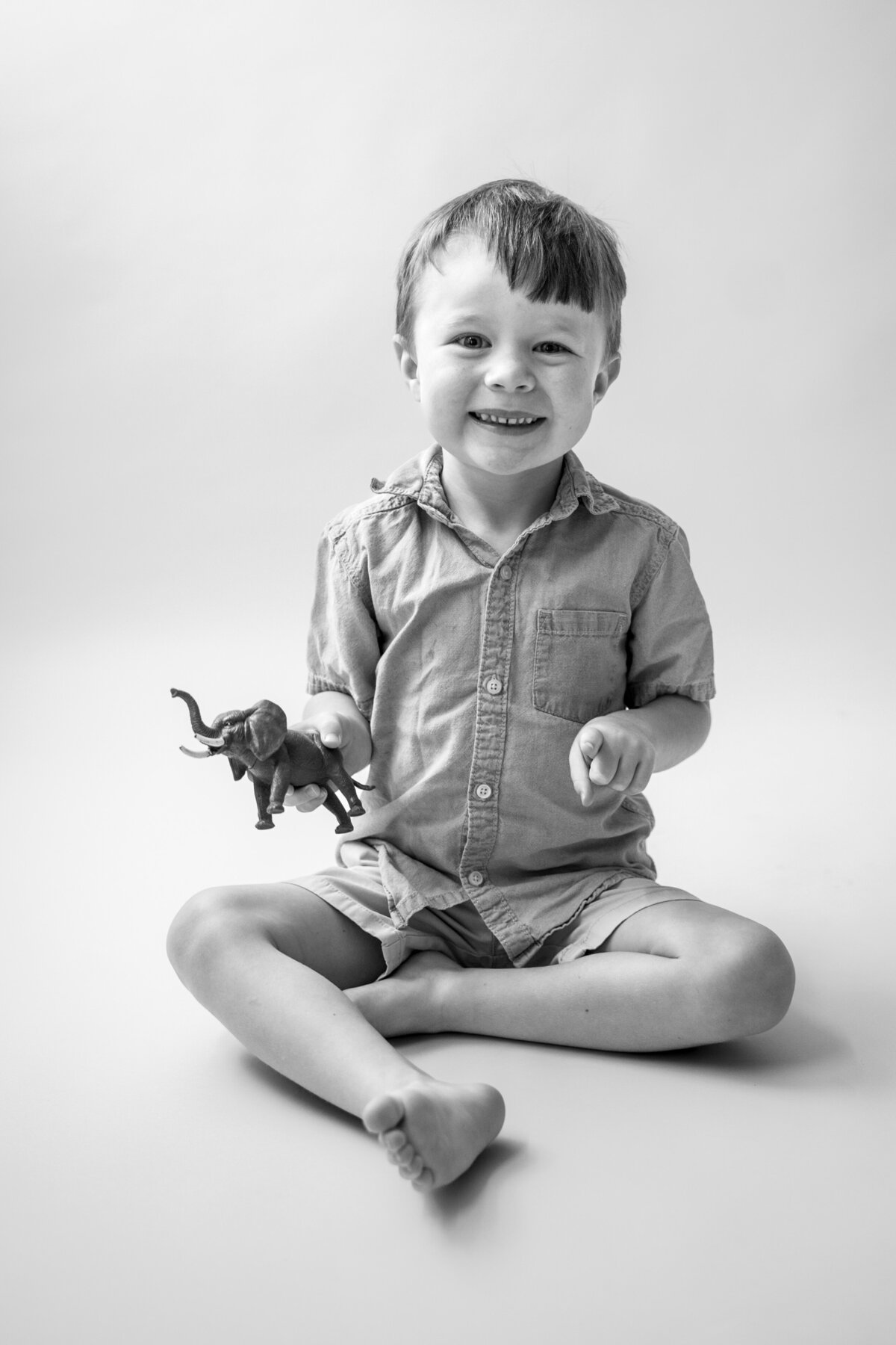 Black and white photo of young boy smiling at camera holding a toy elephant.