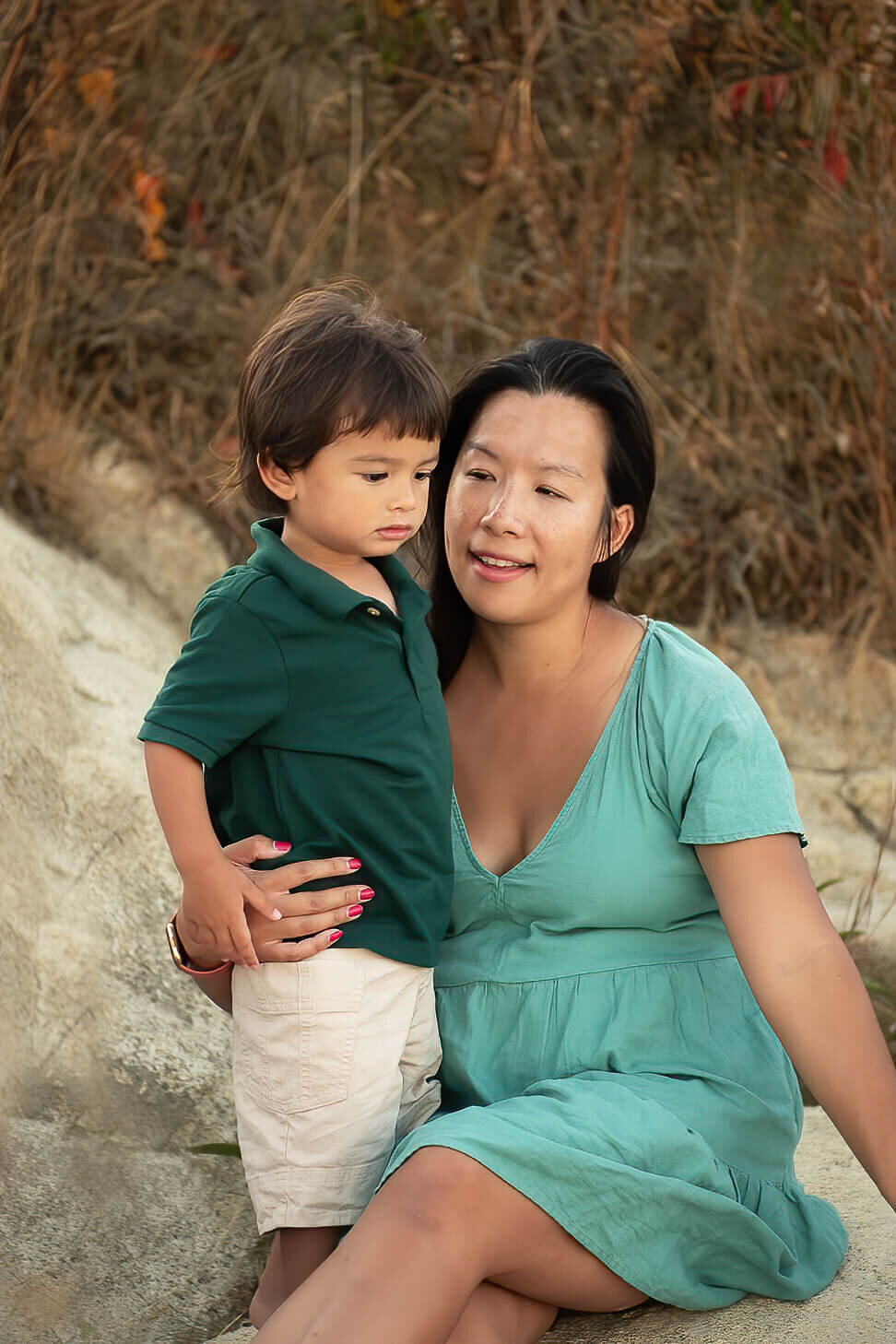 I mom smiles at her young toddler as they sit on the rocks by Wingaersheek Beach.