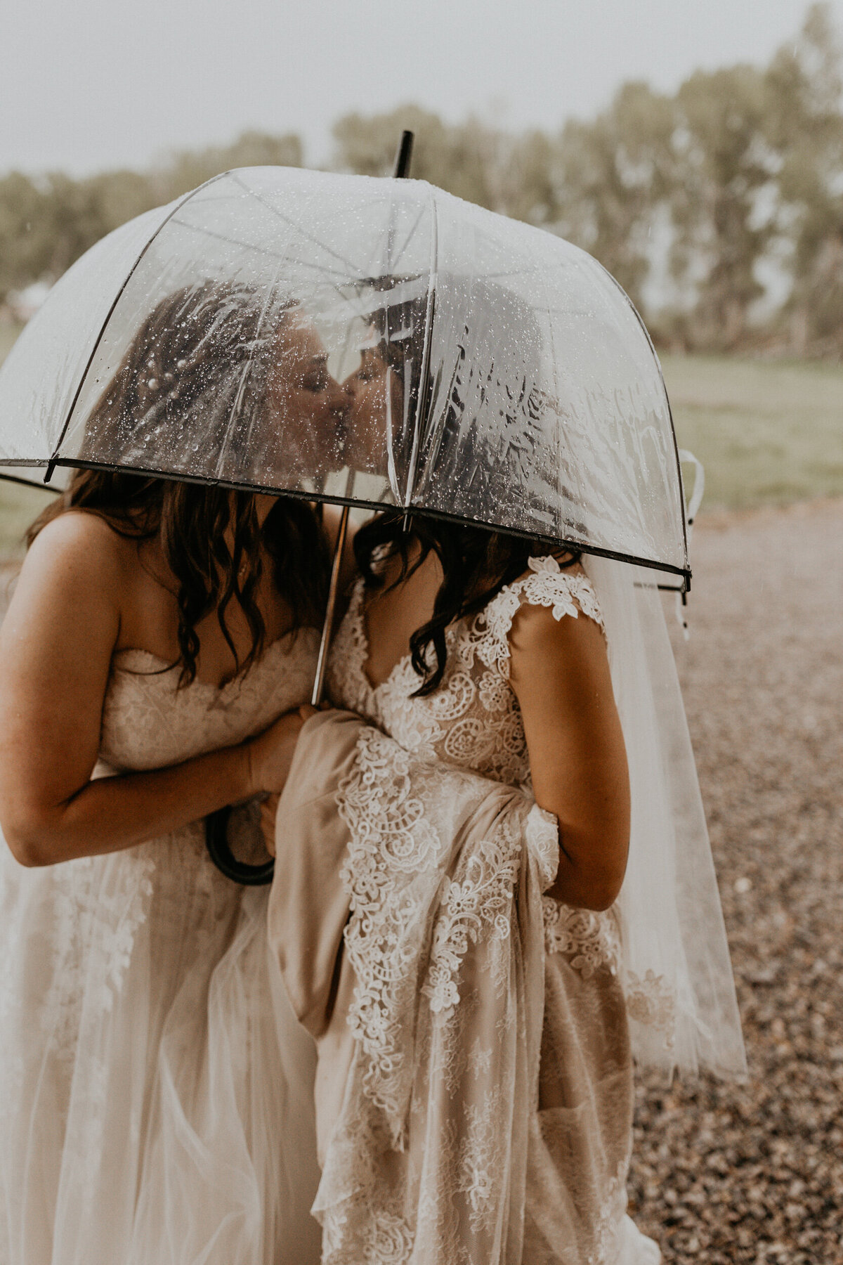 two brides under an umbrella together in the rain kissing
