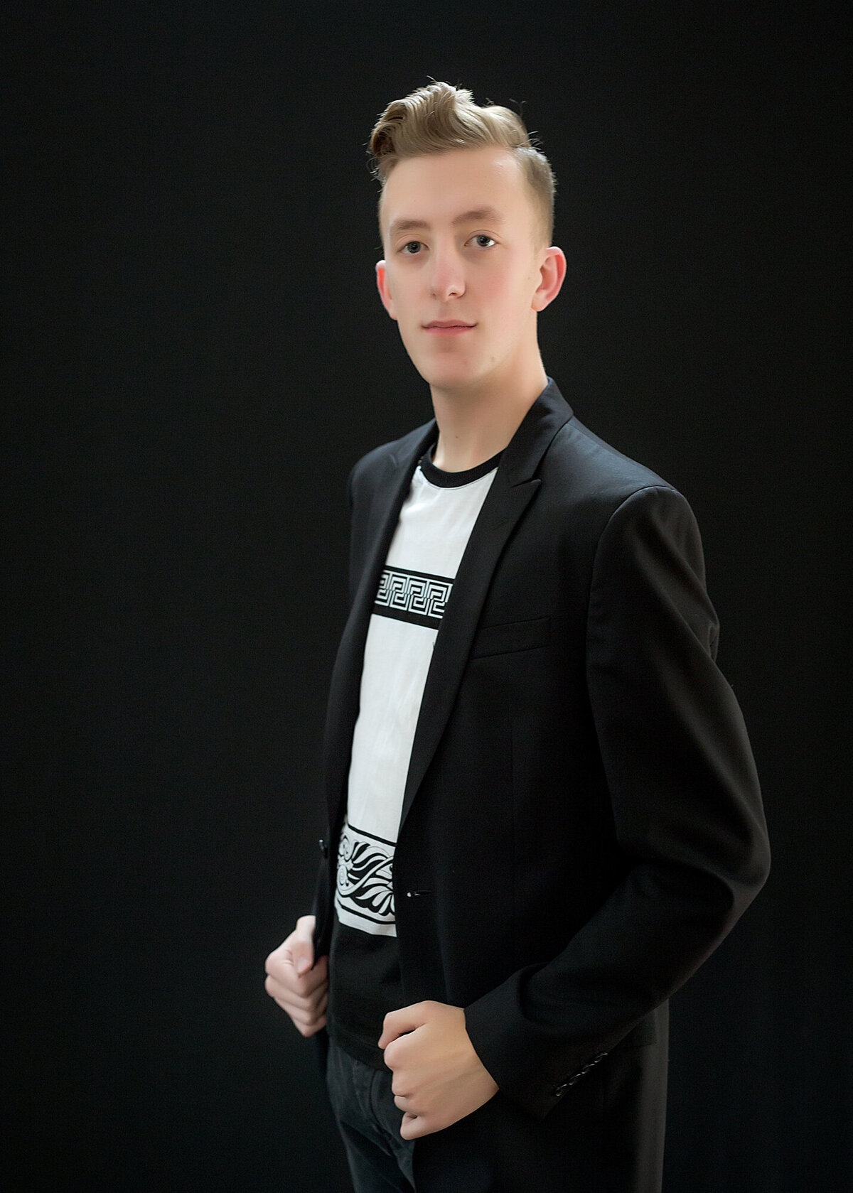 A young male adult headshot client wearing a suit jacket with his hands in belt loops