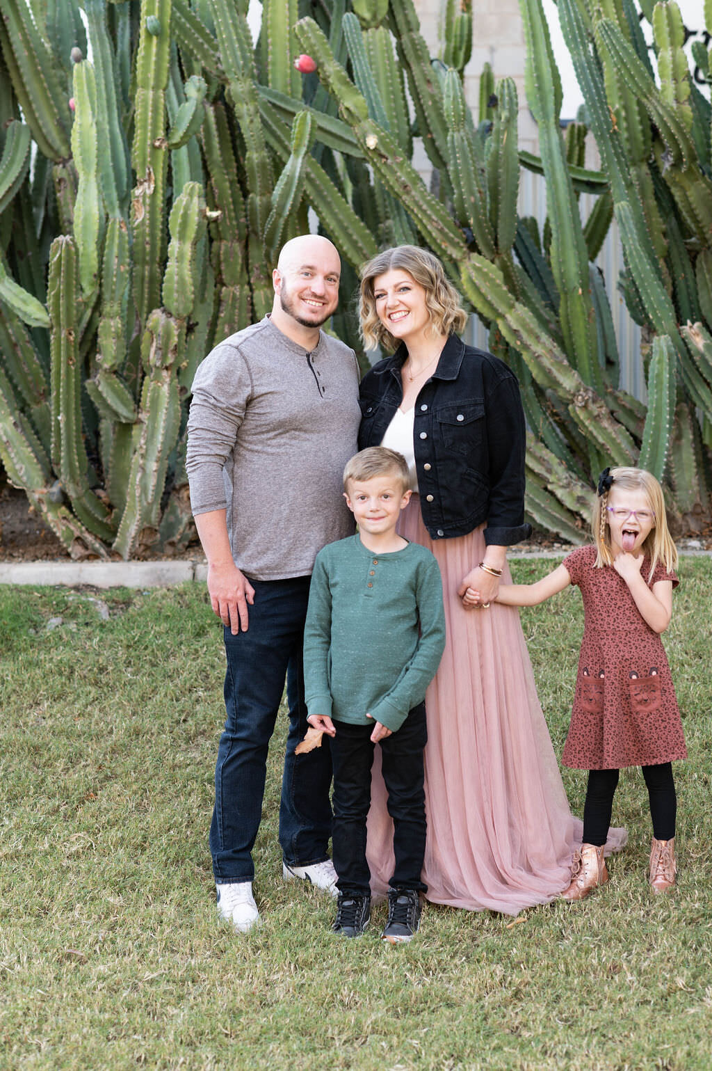 A small family standing in their yard smiling with cacti behind them.