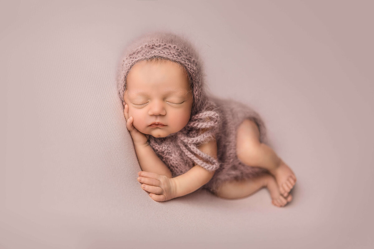 Newborn girl on pink blanket with knit romper and bonnet