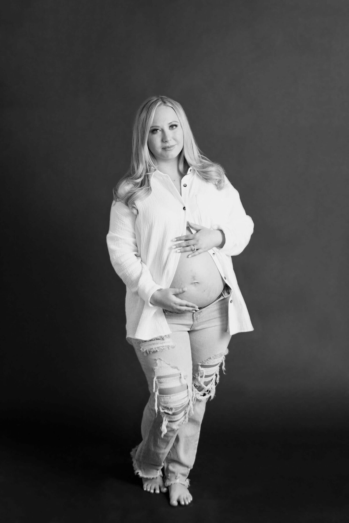 black and white maternity portrait of expecting mother in white button up shirt and jeans