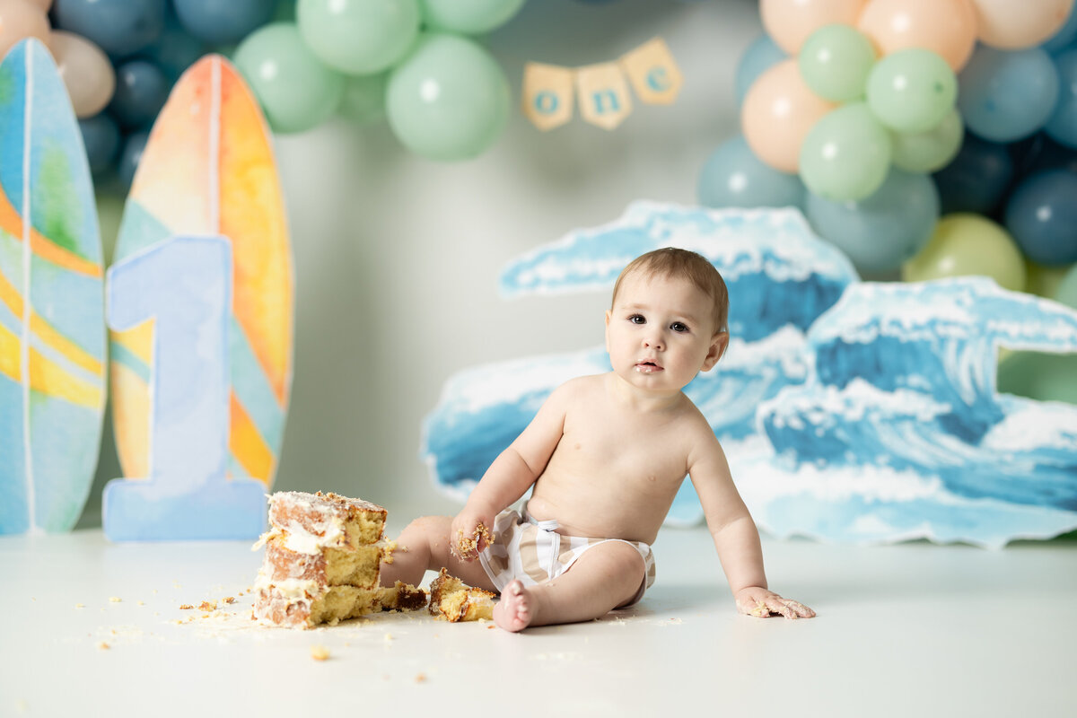 Baby boy with surfboard and wave backdrop for surfing themed cake smash in Canton GA