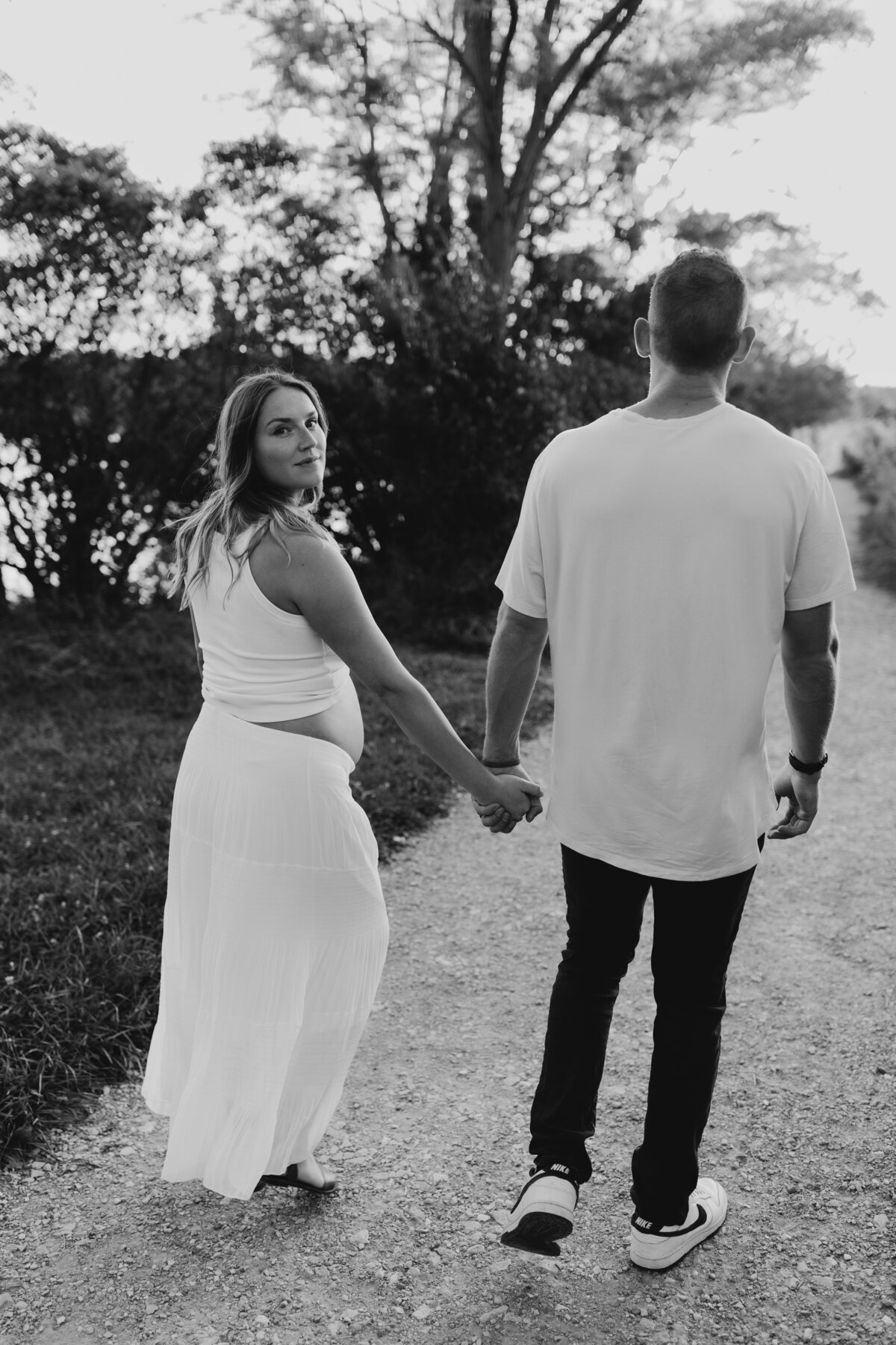 Black and white photo of parents walking on a path, holding hands during a maternity session.