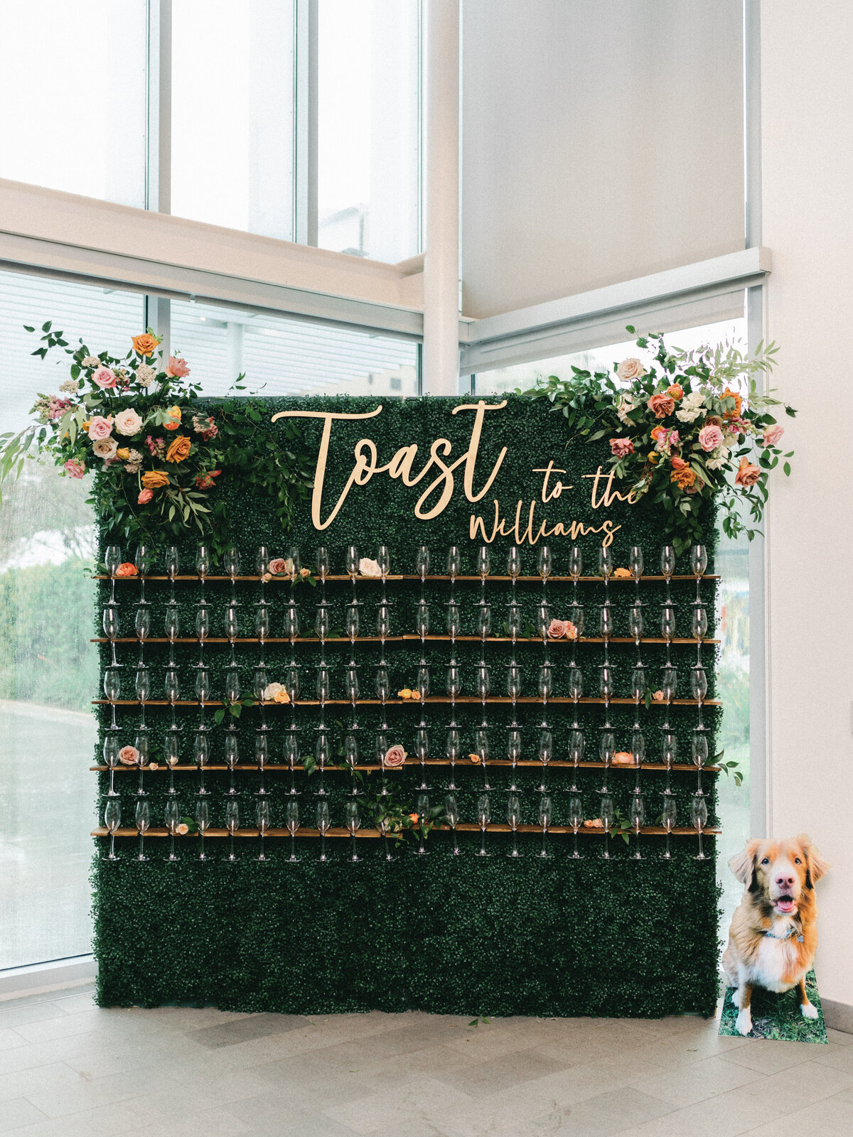 Champagne toast wedding backdrop made of greenery and decorated with florals