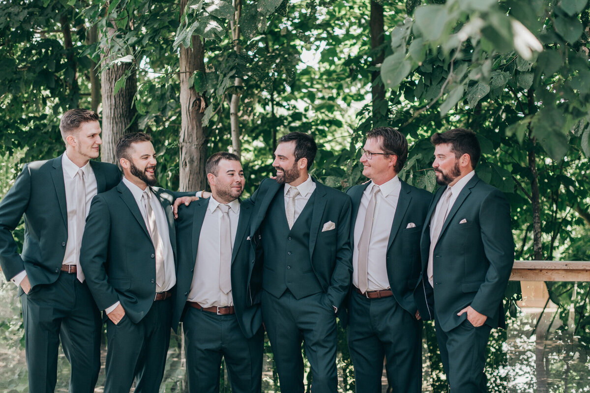 Groom and groomsmen wearing casual green suits posing for a group photo