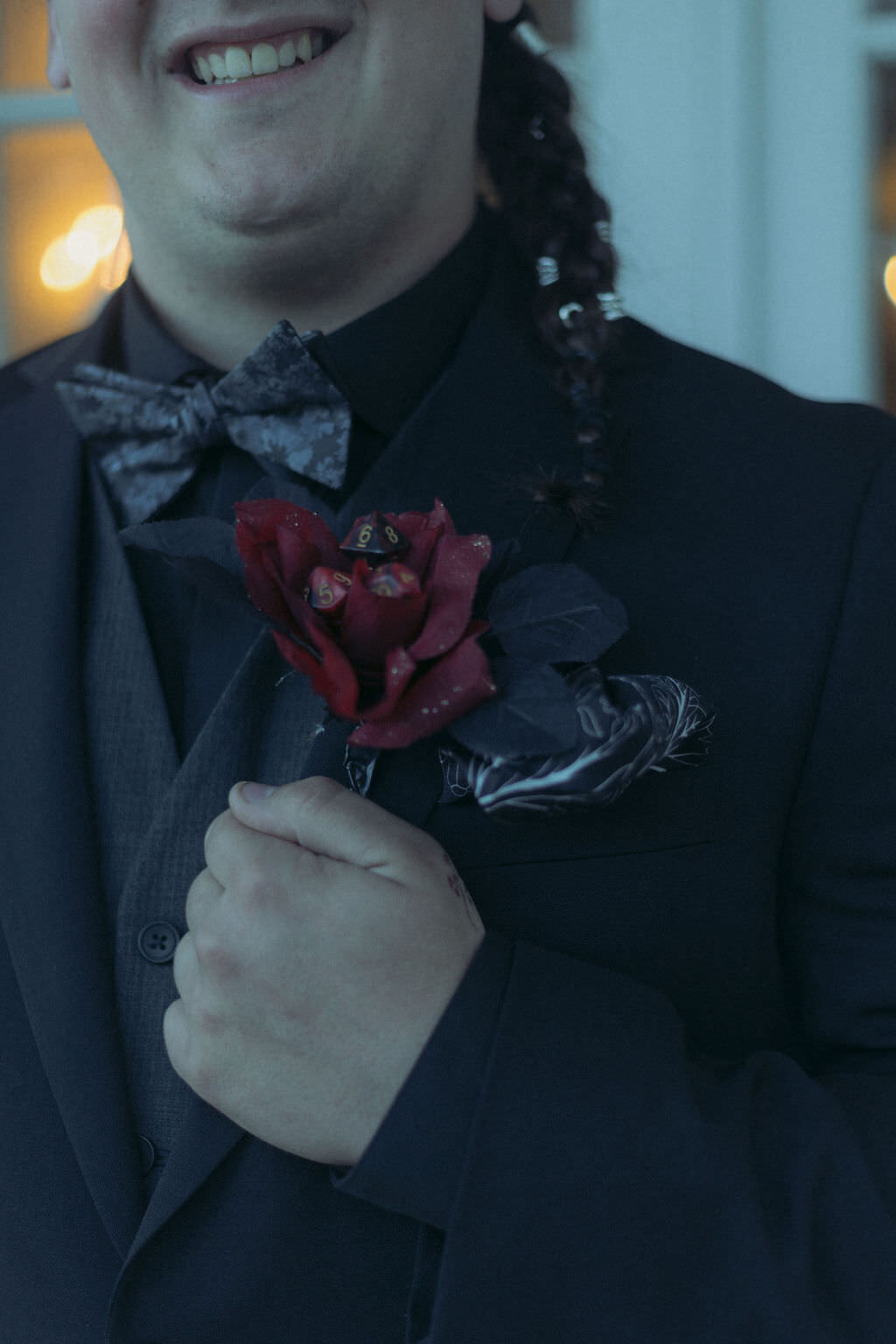 A person holding the collar of their suit jacket with a red flower on it.