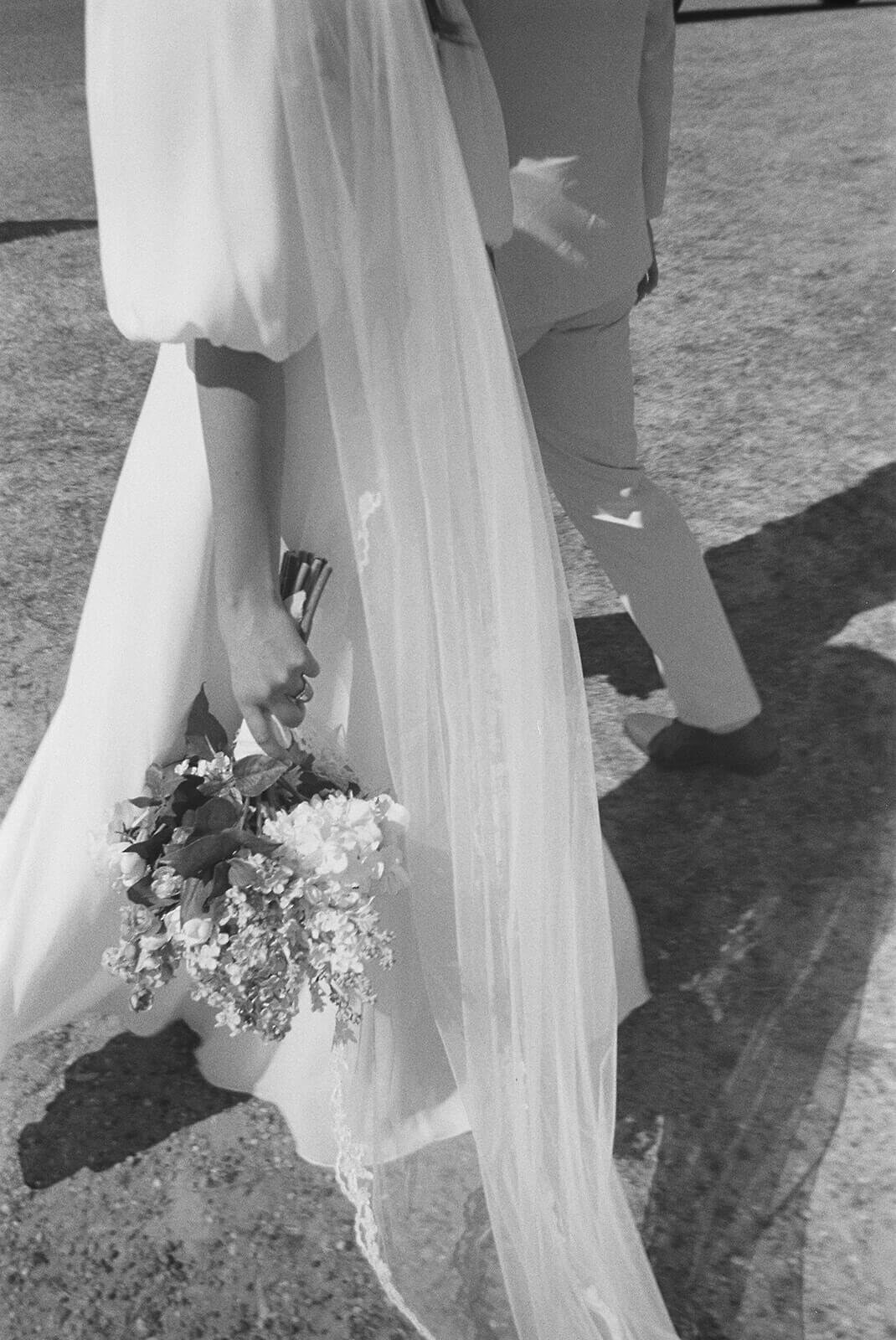 Black and white image of bride and groom walking holding a bouquet.