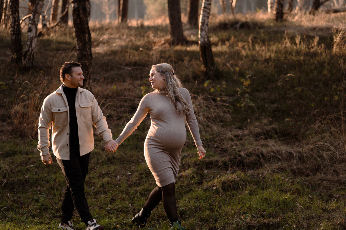 Zwangere vrouw leidt haar man door het bos tijdens een zwangerschapsshoot