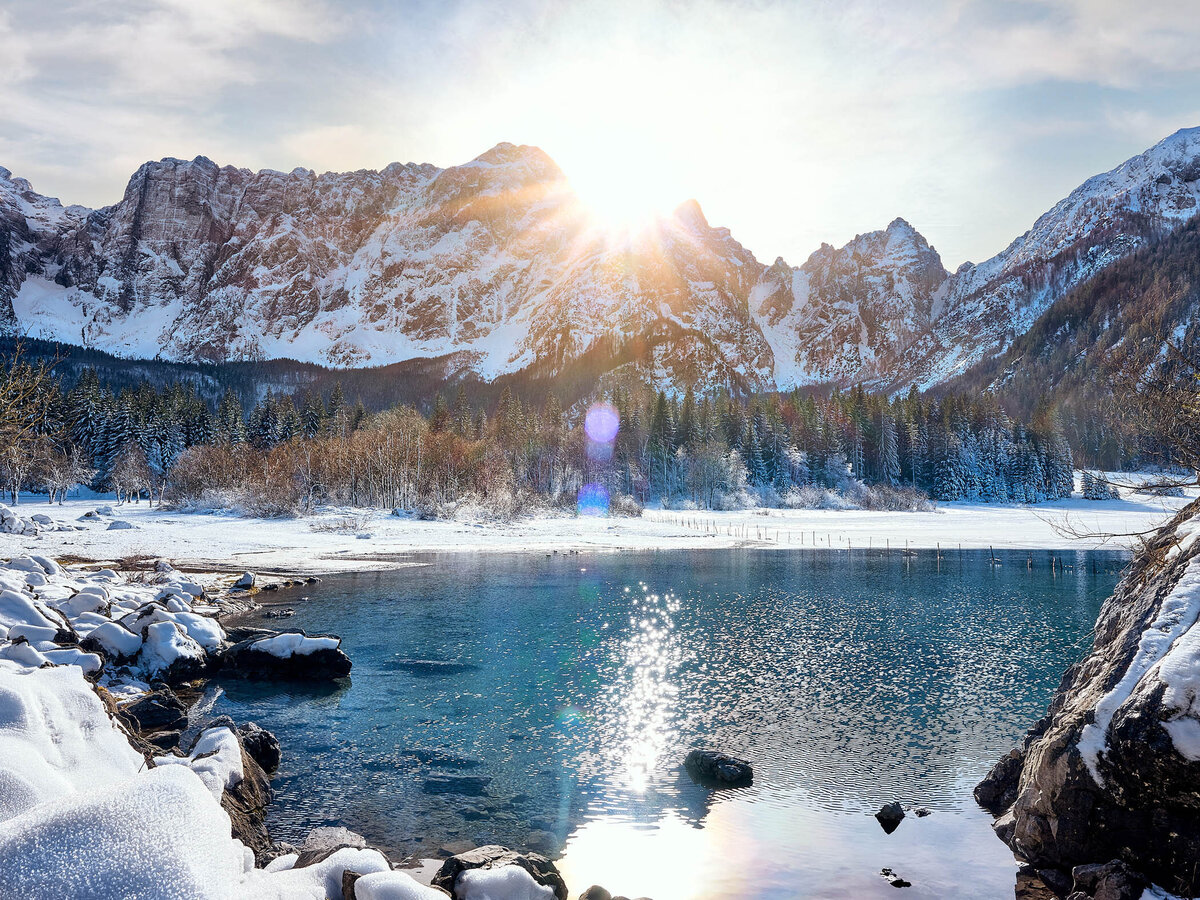 Winterliche Landschaft am Lago di Fusine mit verschneiten Bergen und Sonnenstrahlen – stimmungsvolle Alpenfotografie vom Fotograf Atelier Schulte, tätig in ganz Österreich und Norditalien.